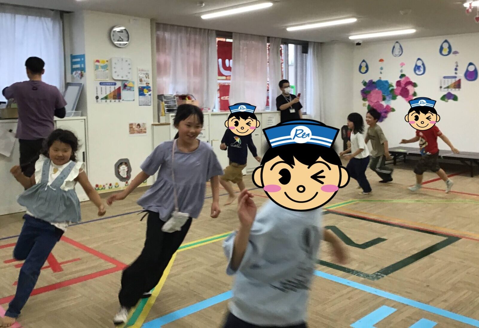 Children running in a school gym during an activity, with colorful floor tape and wall decorations in the background.