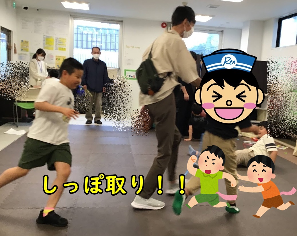 A child runs across a padded play area while adults and other kids watch; cartoon characters and Japanese text cover part of the scene.