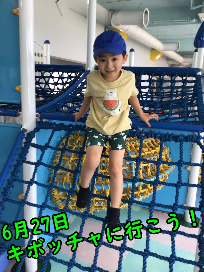 Young child in a yellow shirt and blue cap climbs a blue rope obstacle indoors.