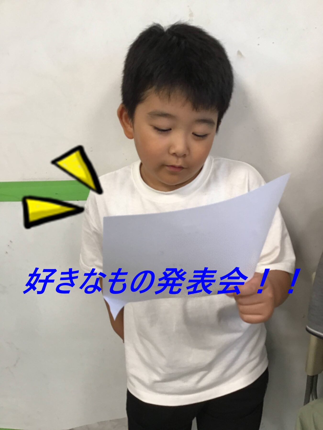 Young boy in a white shirt reads a sheet of paper, as if giving a presentation.