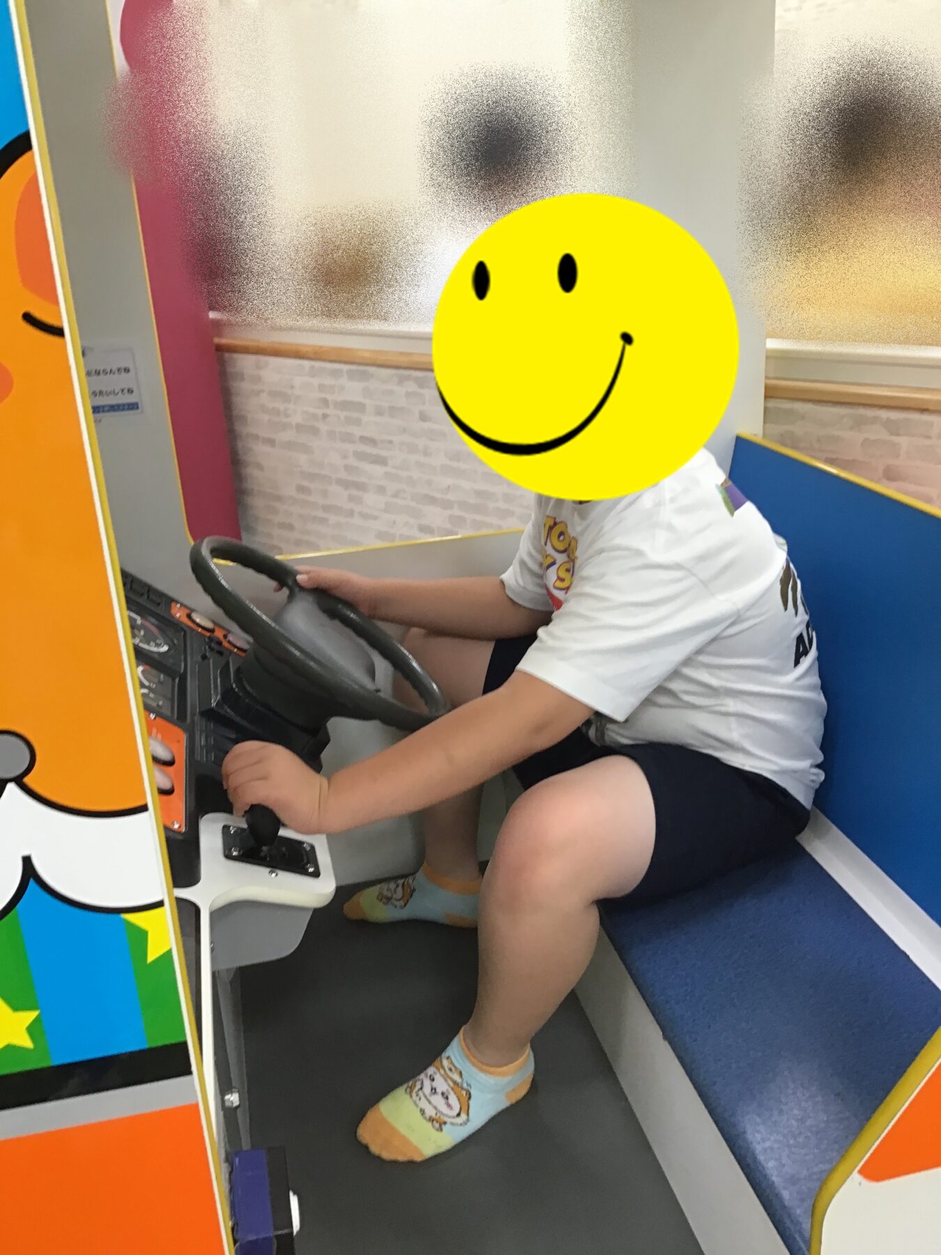 Child sits in a bright arcade driving ride, gripping the steering wheel with both hands.