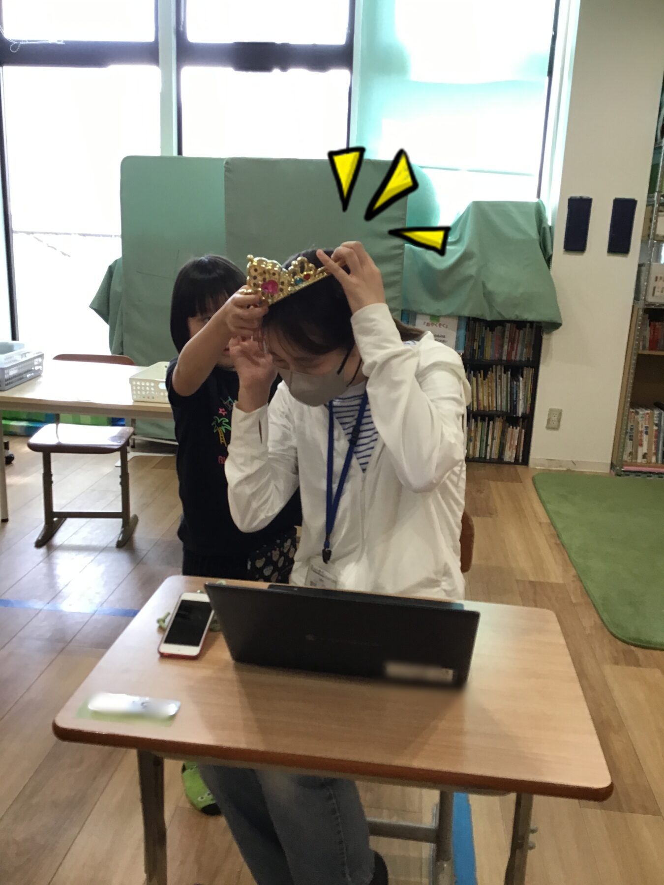 Child helps an adult put a jeweled crown on her head during a classroom activity in a library setting.