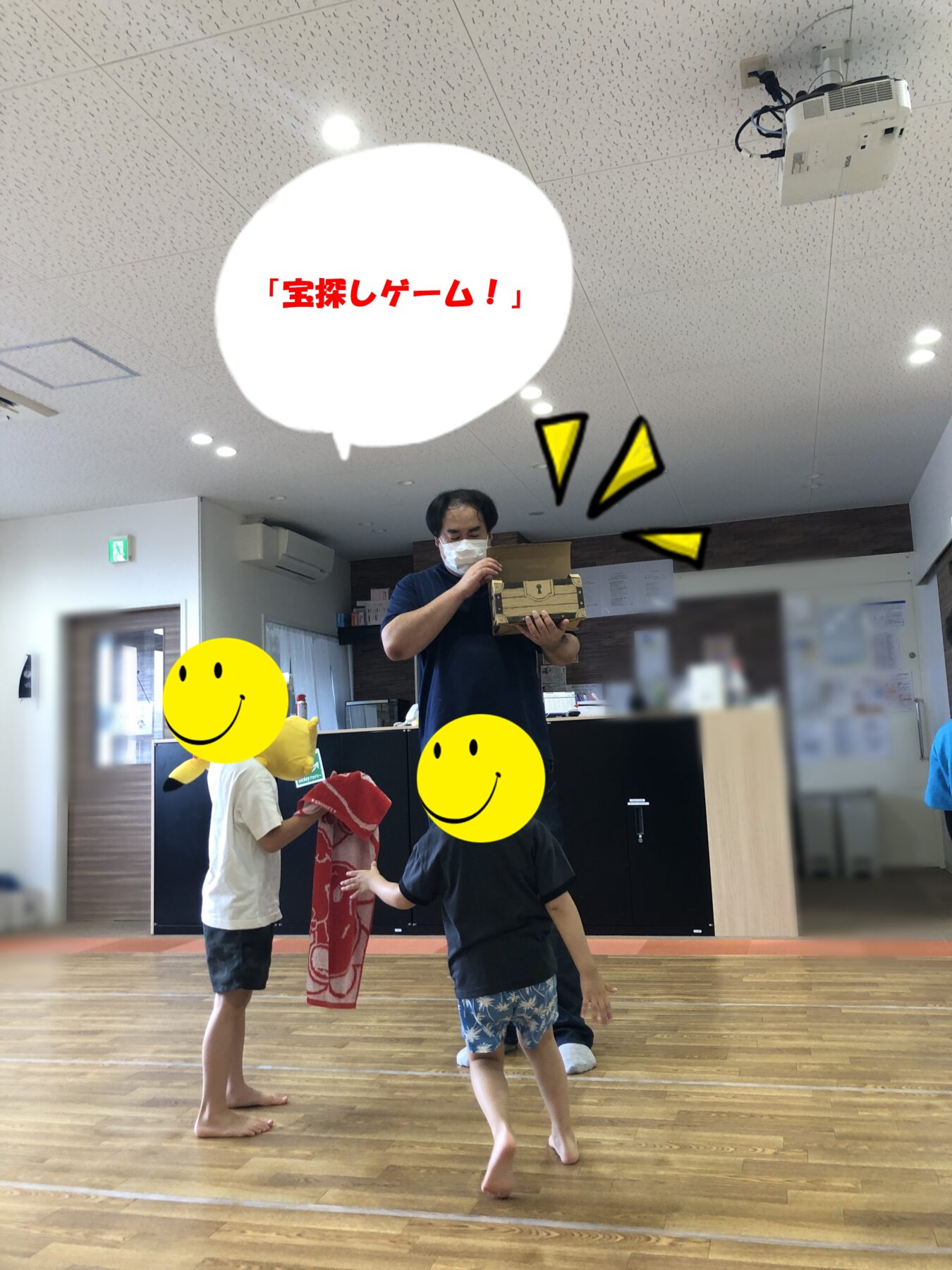 A man wearing a mask holding a cardboard treasure chest while children gather around for a treasure-hunt game indoors, speech bubble reading 'Treasure Hunt Game!'