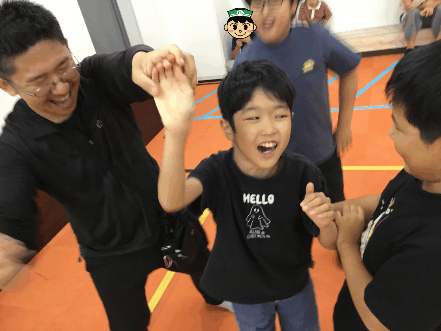 A smiling boy in a black shirt high-fives teammates in a gym with an orange floor and blue lines behind him