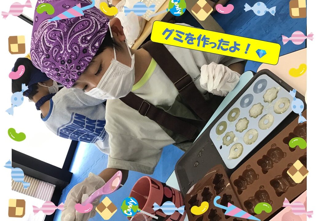 Children wearing masks and bandanas make gummy candies in donut molds, with a bright yellow banner reading 'We made gummies!' and candy-themed border around the scene.