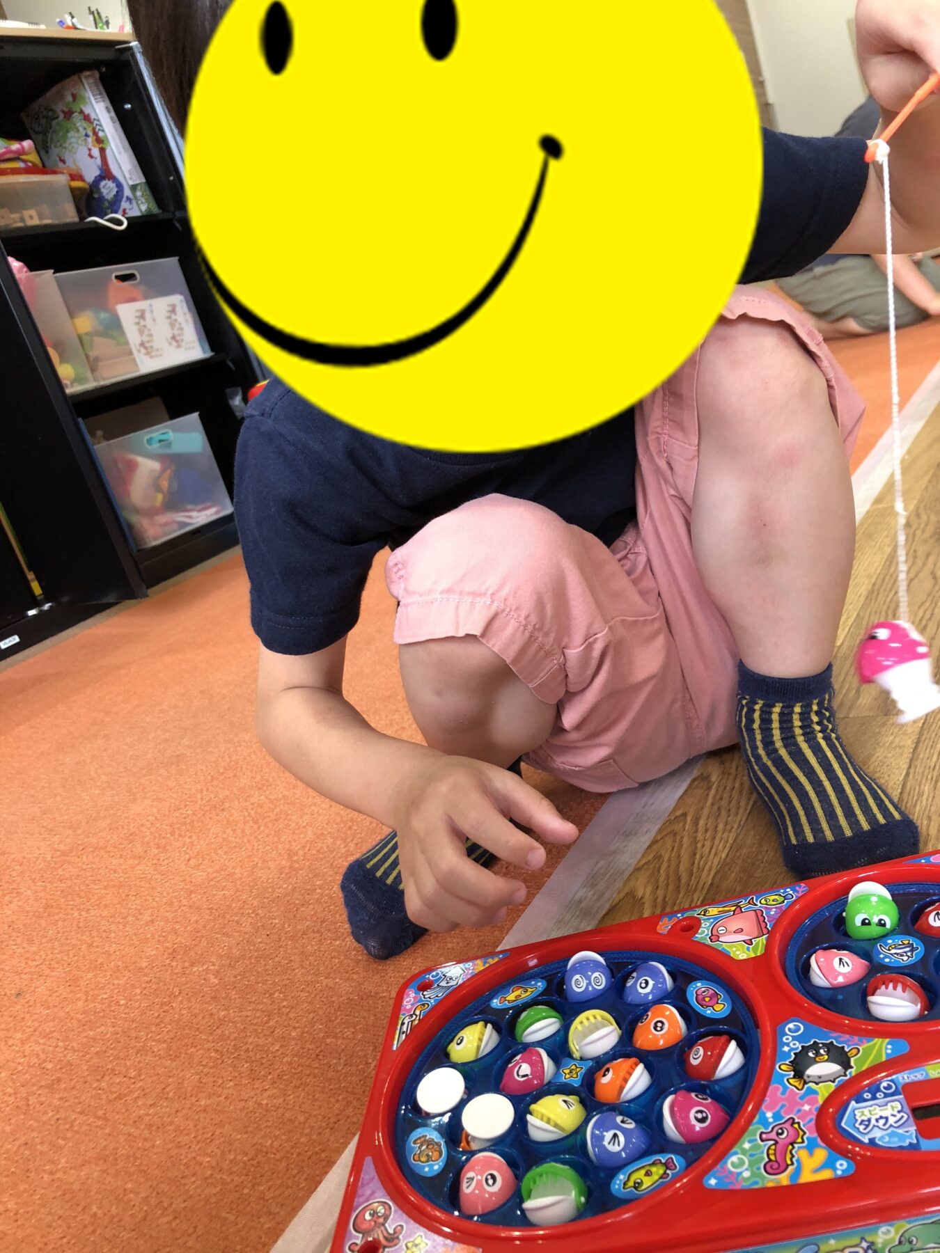 Child kneels on an orange carpet, playing with a colorful bead maze toy in a classroom setting.