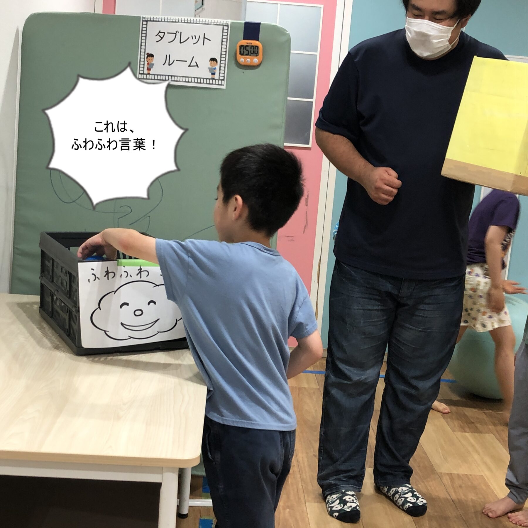 子どもが箱型の玩具を操作している室内の遊び場。壁の看板に『タブレットルーム』と表示されている。
