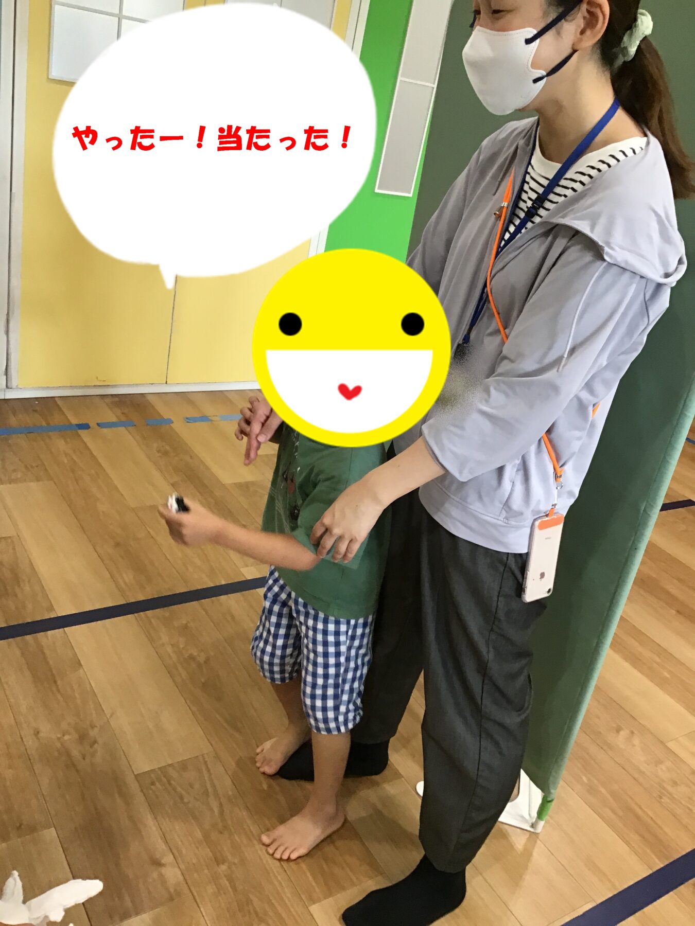 Staff member in a mask helps a child in an indoor gym; speech bubble reads 'やったー!当たった!'