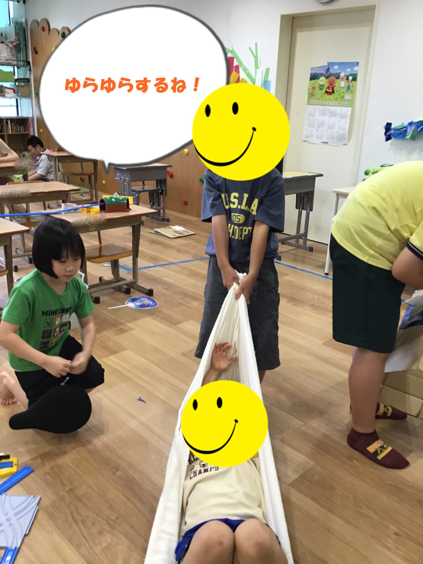 Children in a bright classroom play with a white fabric hammock while others sit at desks nearby.