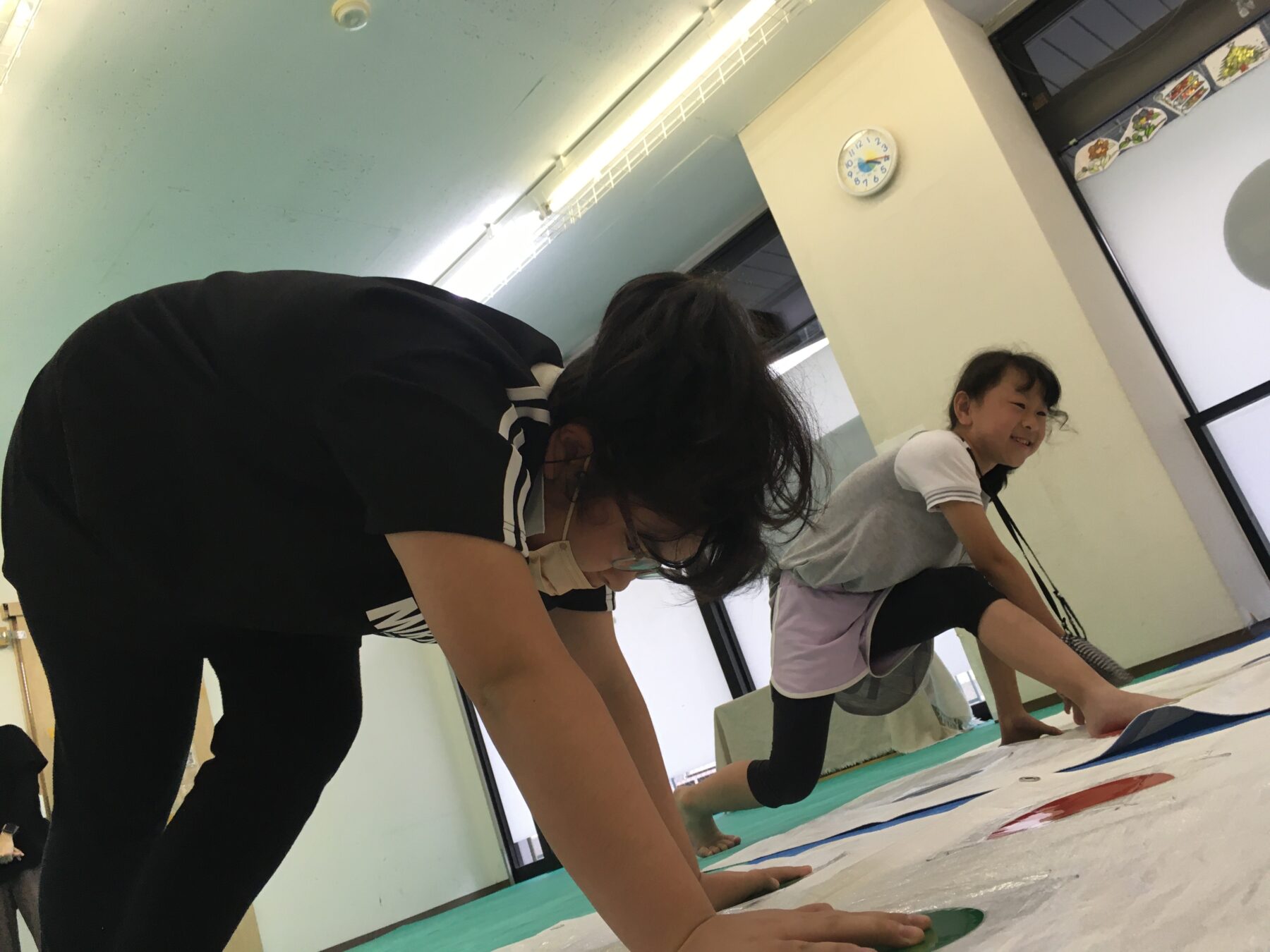 Two children in a classroom doing a floor-mat activity, leaning forward on their hands and knees.