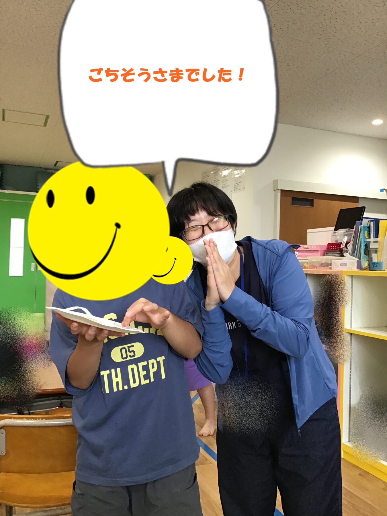 Two people indoors; one bows with hands pressed together (a mask on) while the other holds a paper, a large yellow smiley sticker covers part of the scene, and a speech bubble reads 'ごちそうさまでした!'