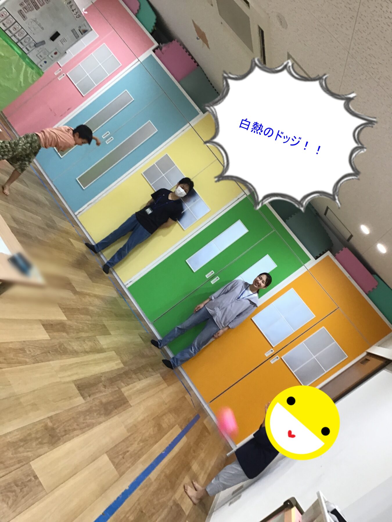 Three people stand in a pastel, color-blocked room with door murals; one person wears a mask while posing for the photo.
