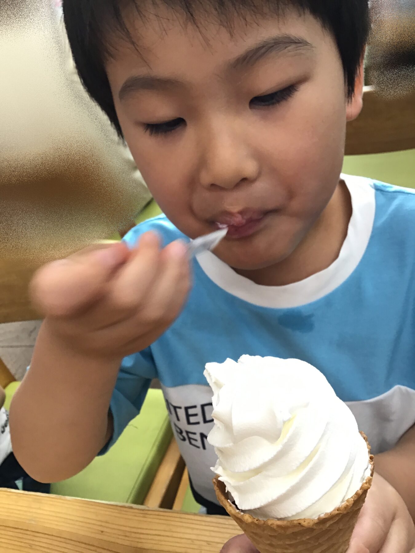 Child smiling softly while licking a vanilla soft-serve ice cream cone held up close to the camera.