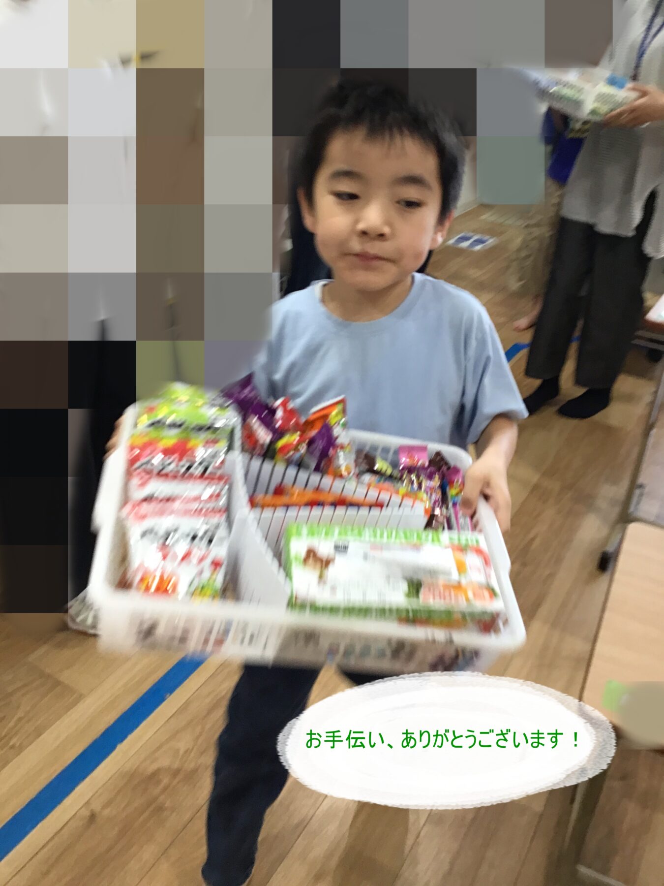 Young boy in a light blue shirt carries a basket filled with assorted colorful snacks in an indoor setting.
