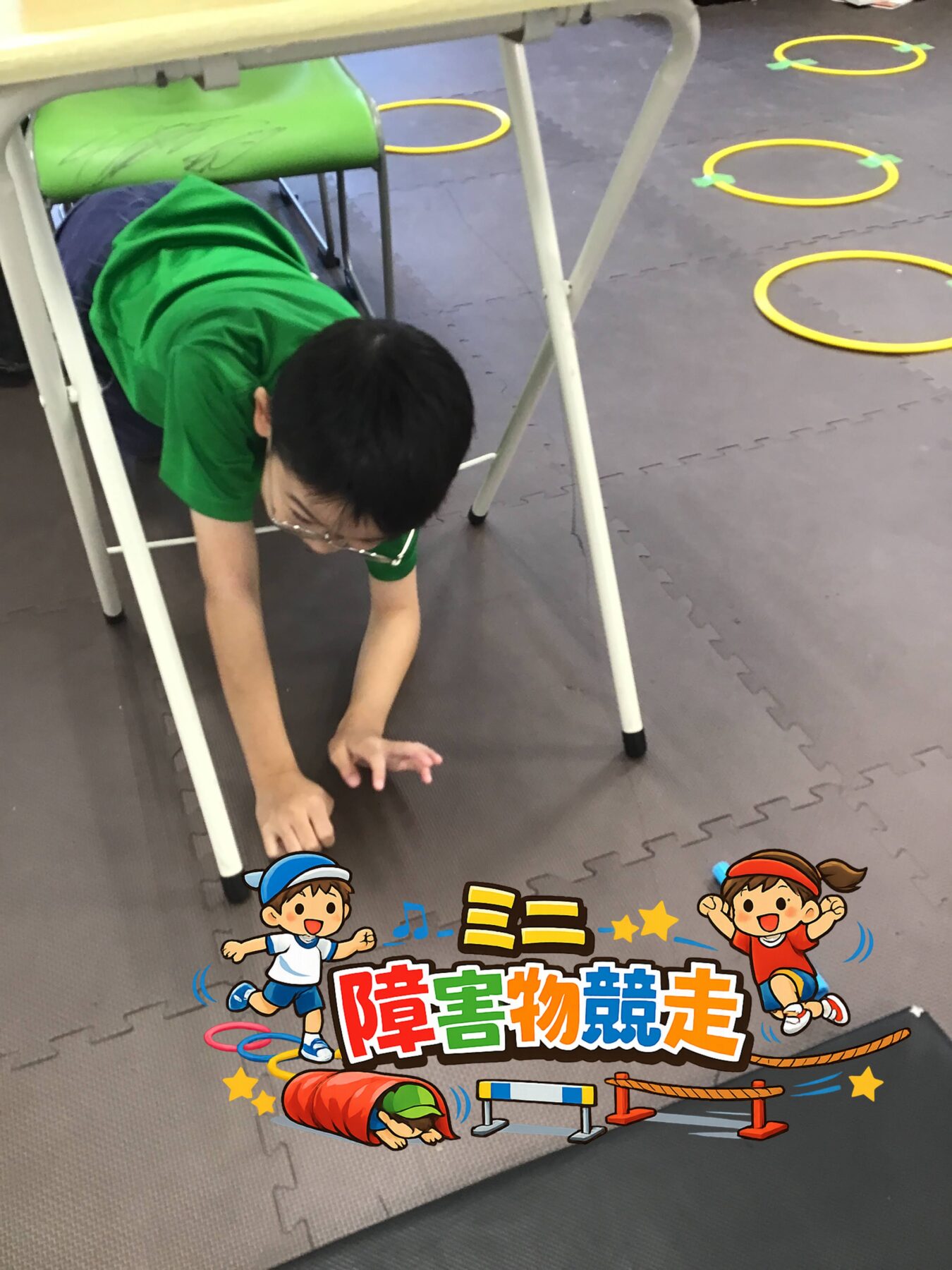 Child in a green shirt crawls under a table as part of an indoor obstacle course on foam mat with yellow circular markers.