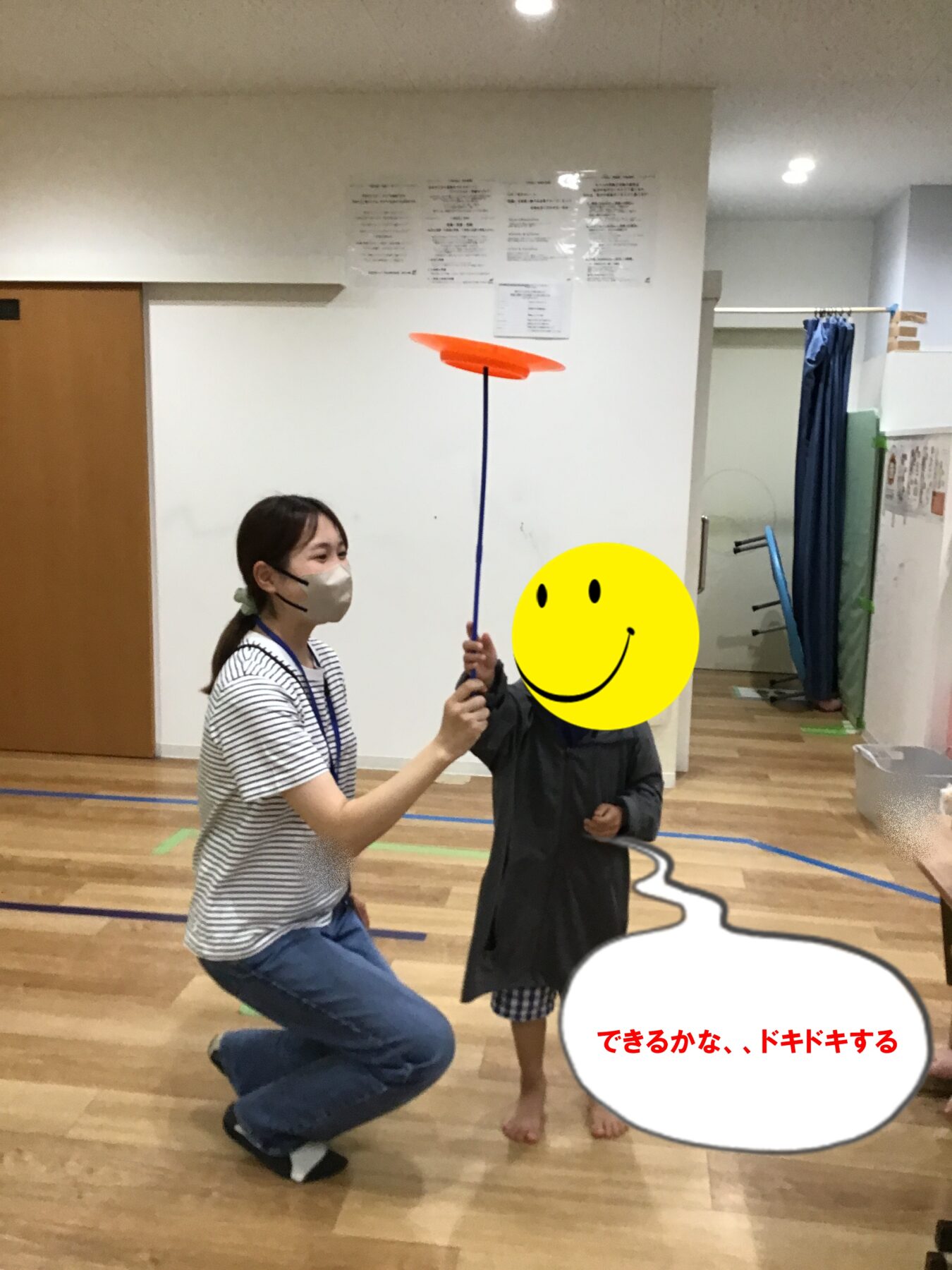 Adult and child indoors playing with an orange disc on a blue pole, guiding a pose or spin activity in a gym setting.