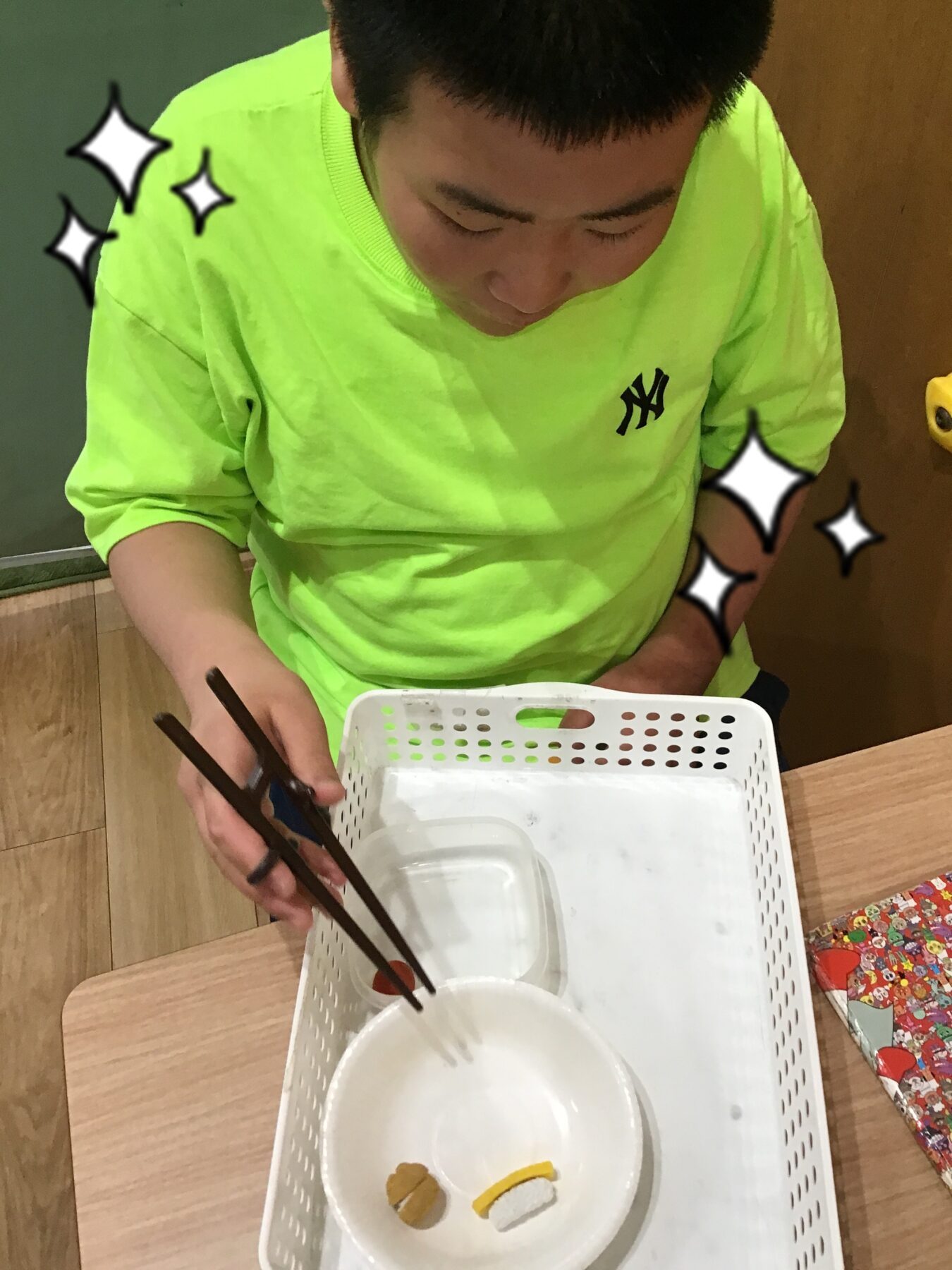 Person in a neon green shirt uses chopsticks to pick up food from a white bowl inside a perforated basket at a table.