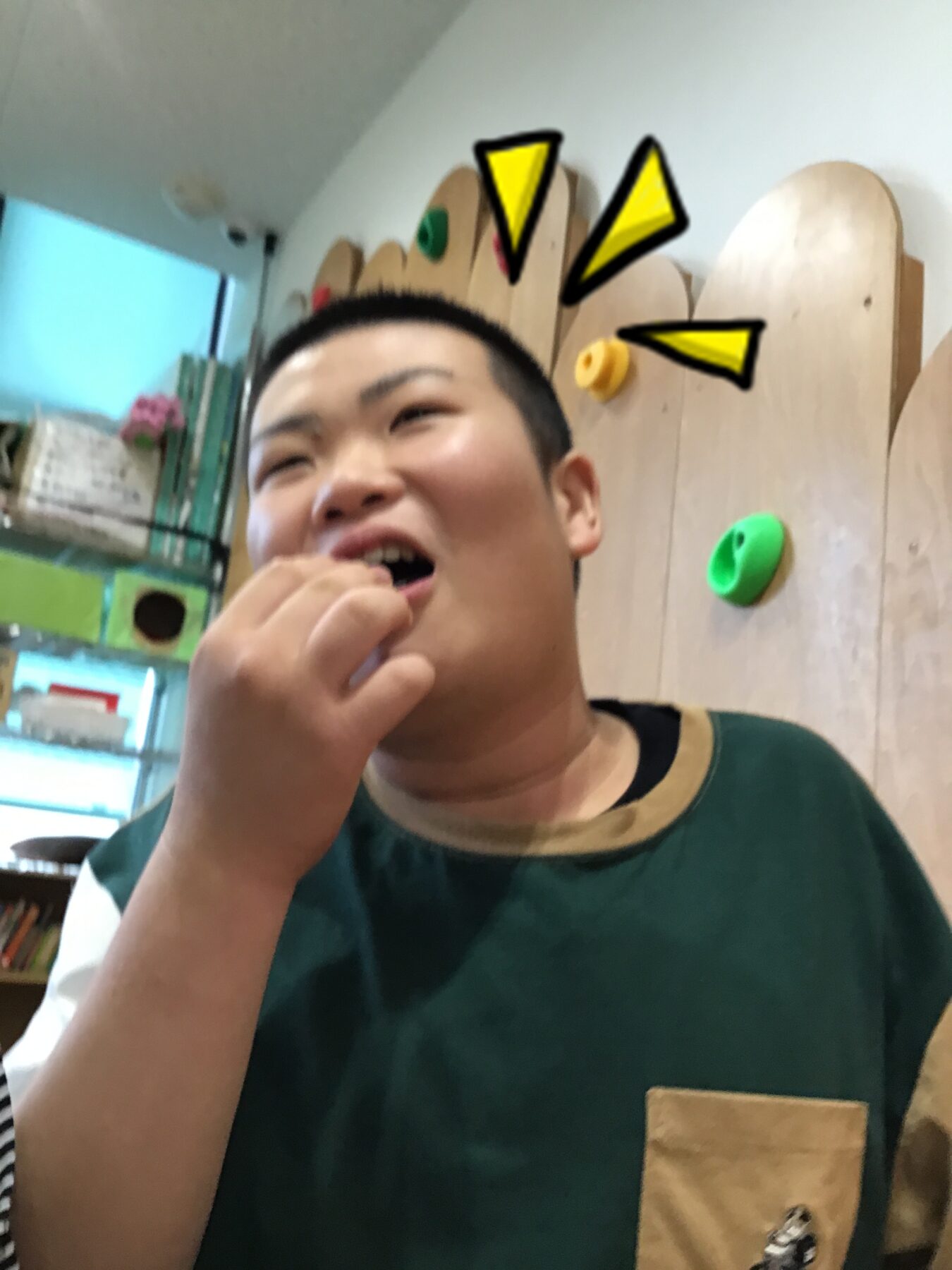 Person with hand near mouth in an indoor climbing gym, colorful holds on a wooden wall behind.