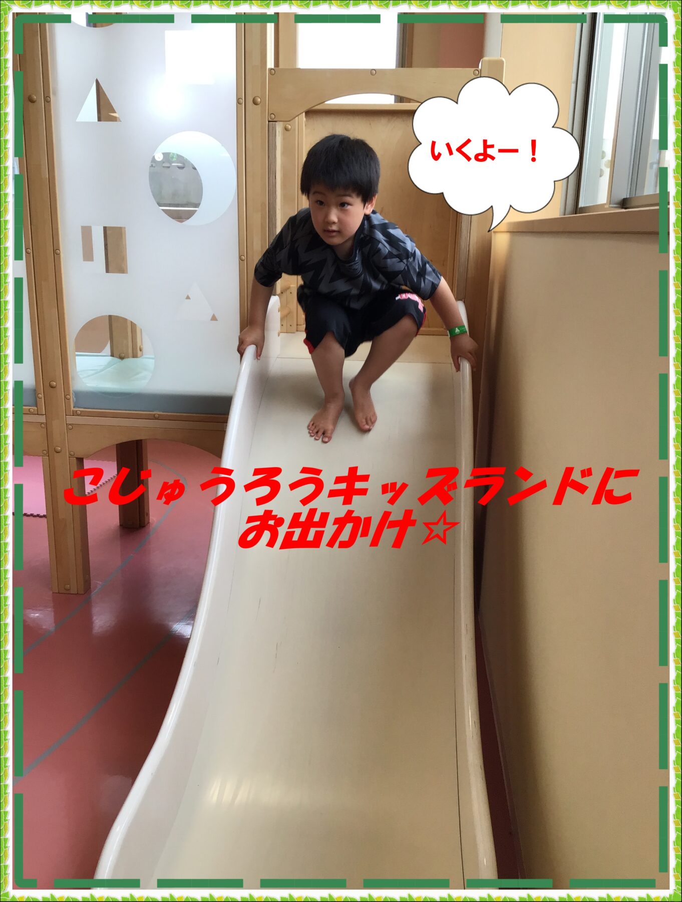 Young boy crouched on a white indoor slide, about to slide down in a kids' play area; speech bubble reads 'いくよー！'