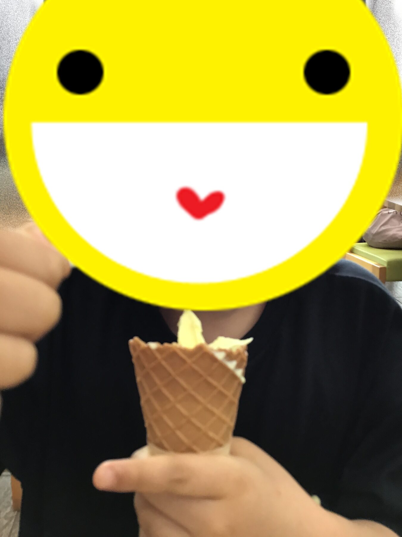 Person in a dark shirt holding a waffle cone with ice cream, with a large yellow smiling emoji obscuring their face.