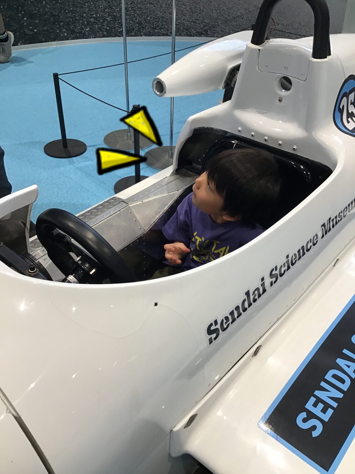 A child sits in a white, single-seat cockpit of a small sci‑tech vehicle at a science museum exhibit.