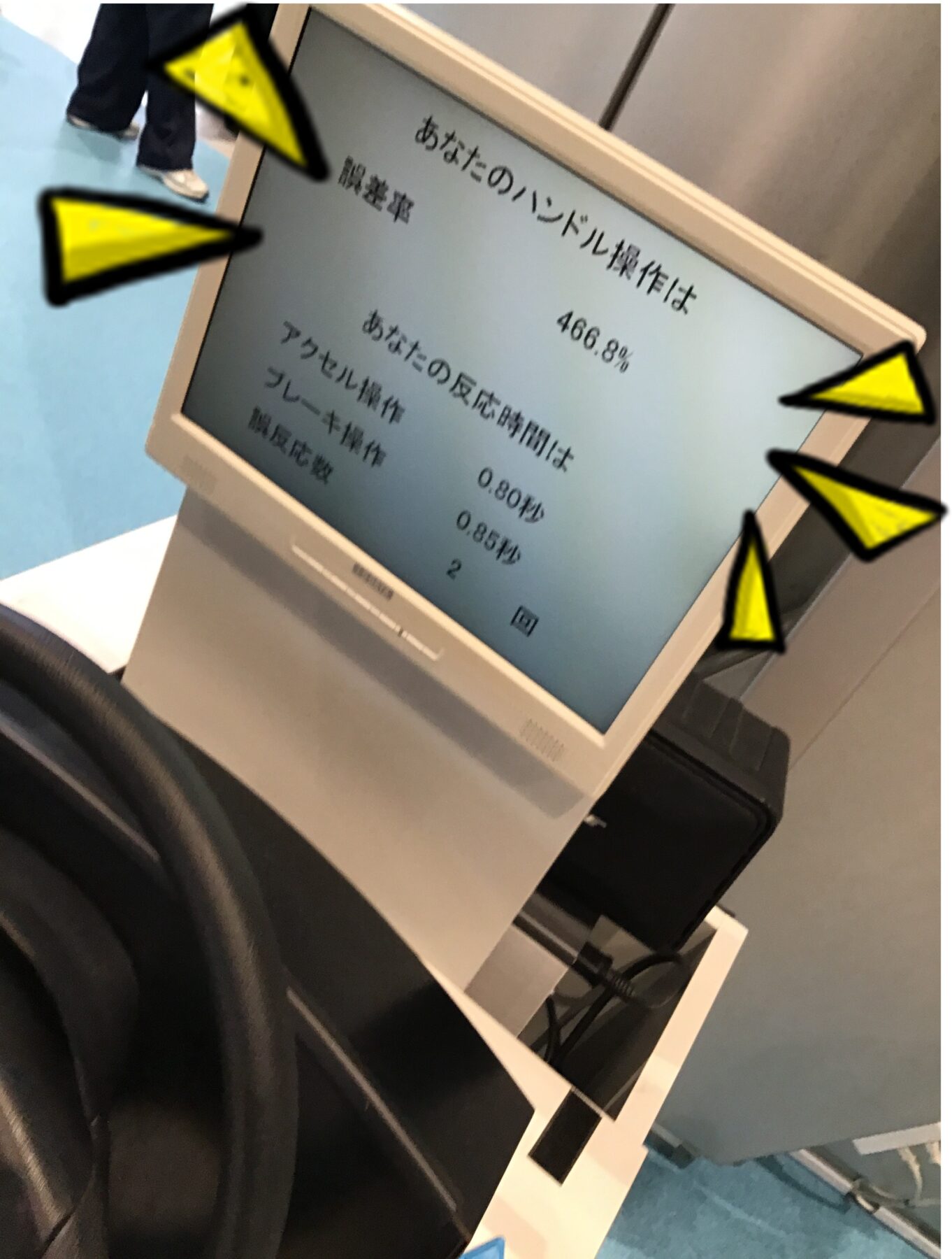 Tilted computer monitor displaying Japanese text and numbers, with yellow arrow annotations pointing at the screen in a workspace.