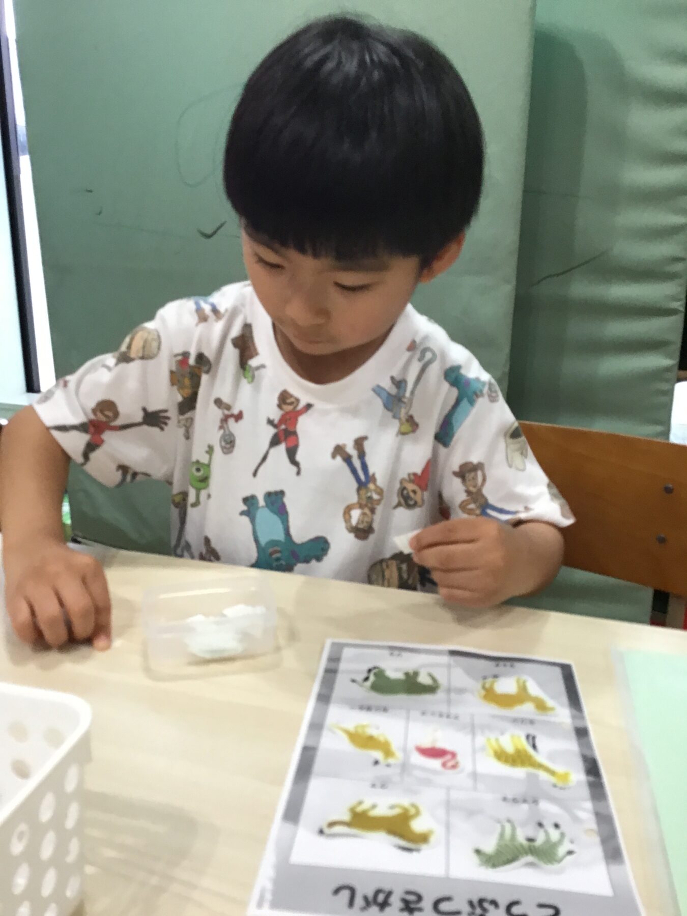 Young boy sits at a table, looking down as he places dinosaur stickers on a worksheet.