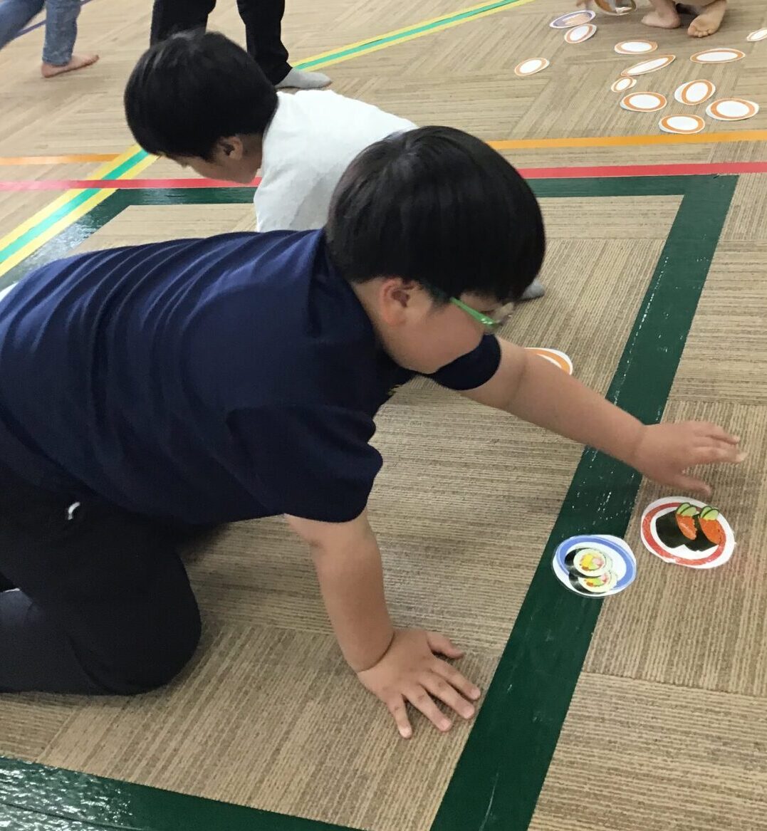 Group of children playing a floor game in a gym, collecting round orange-bordered cards laid on the floor.