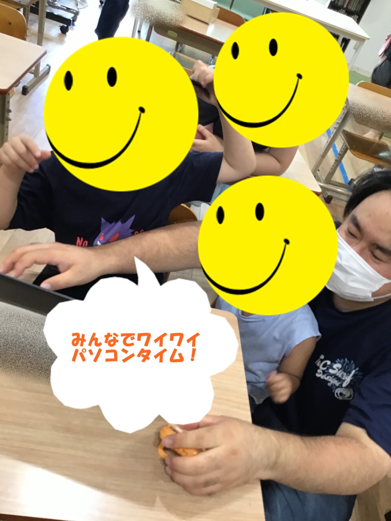 Three people gathered around a laptop at a classroom desk, smiling as they work together; one person wears a mask. A white speech bubble with orange Japanese text sits in the foreground: 'みんなでワイワイパソコンタイム!'