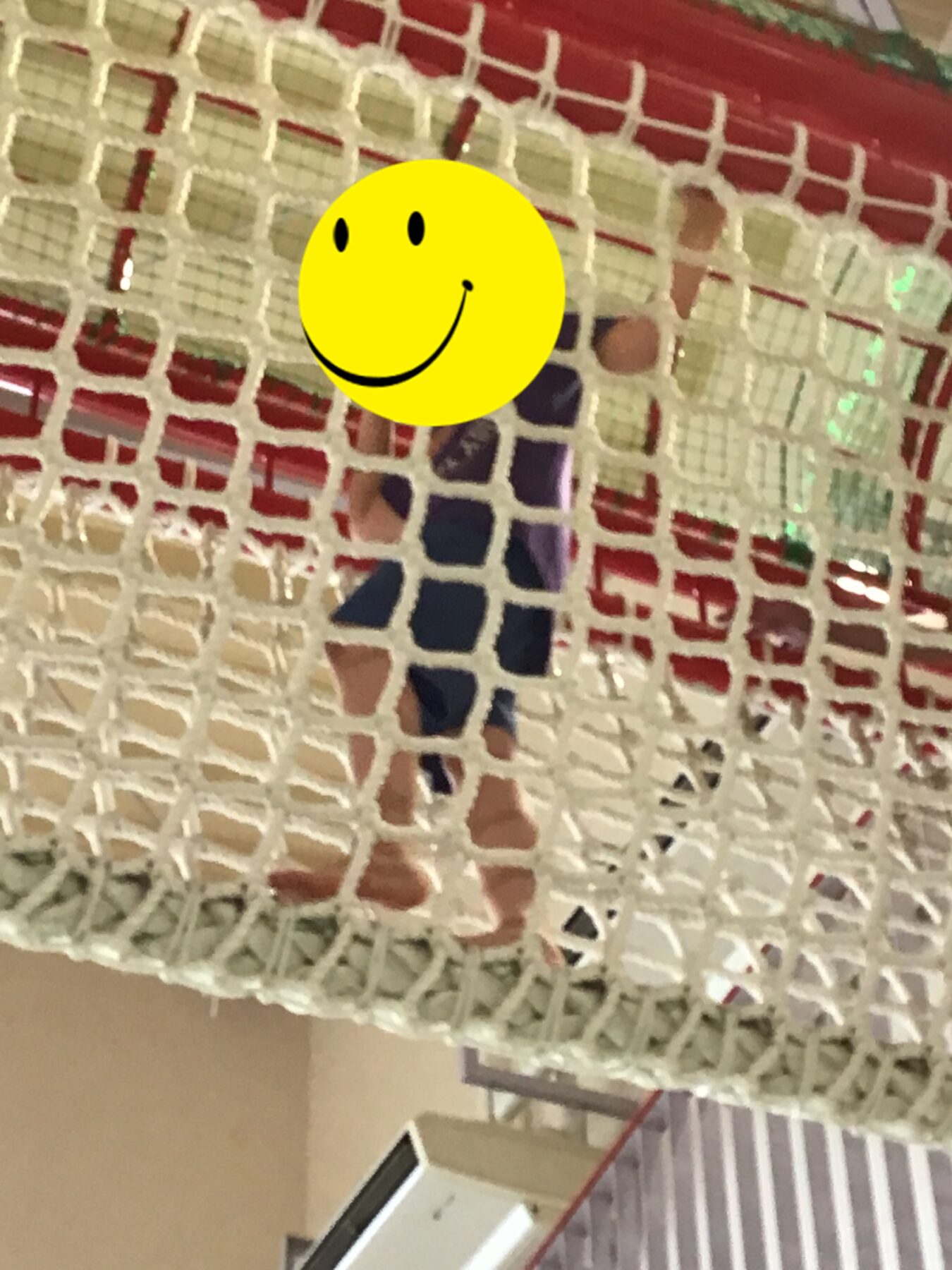 Person standing behind a white plastic lattice barrier in a hallway, with a yellow smiley sticker covering their face