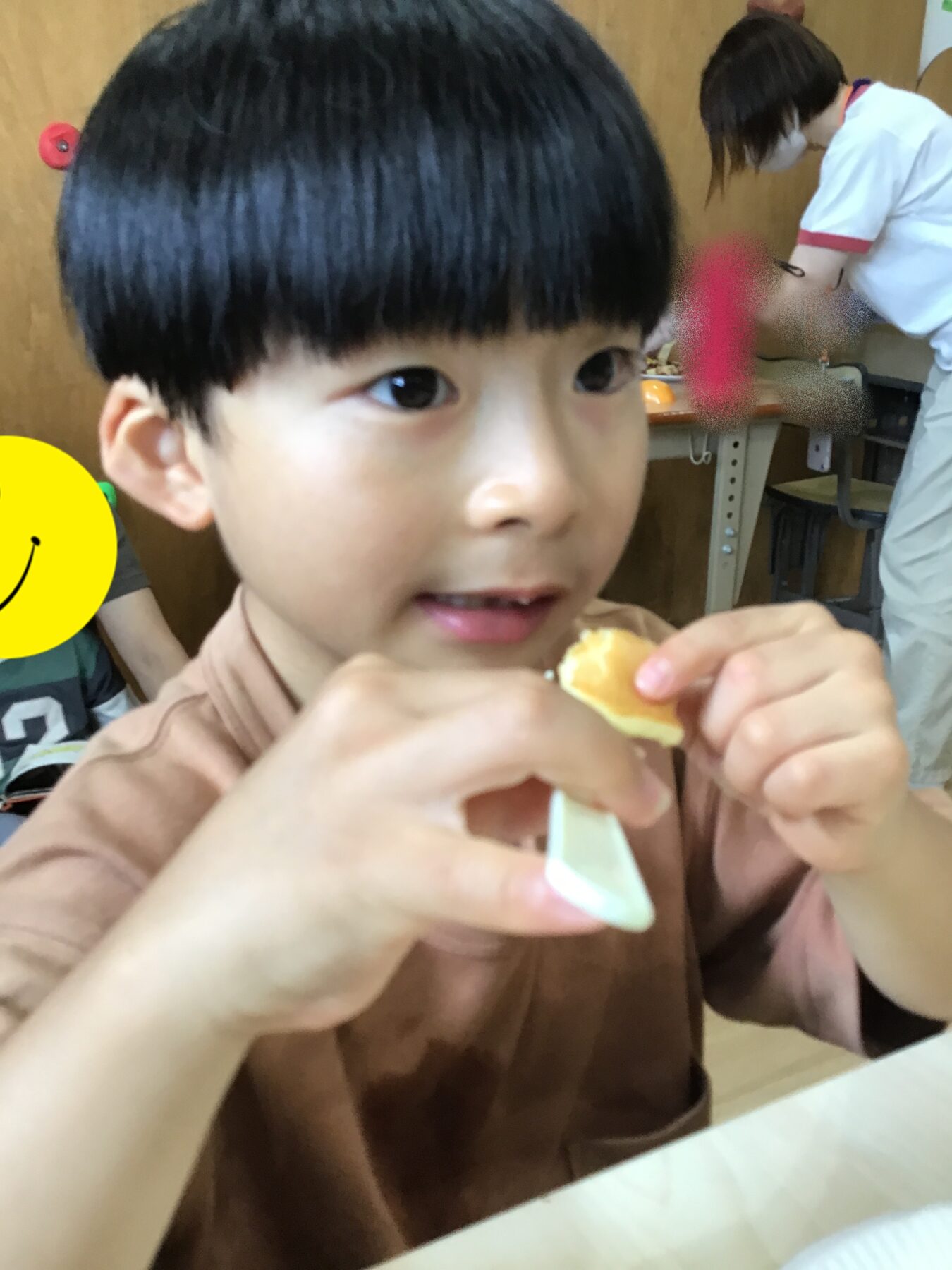 Close-up of a young boy with dark hair biting into a piece of bread, hands in the foreground.