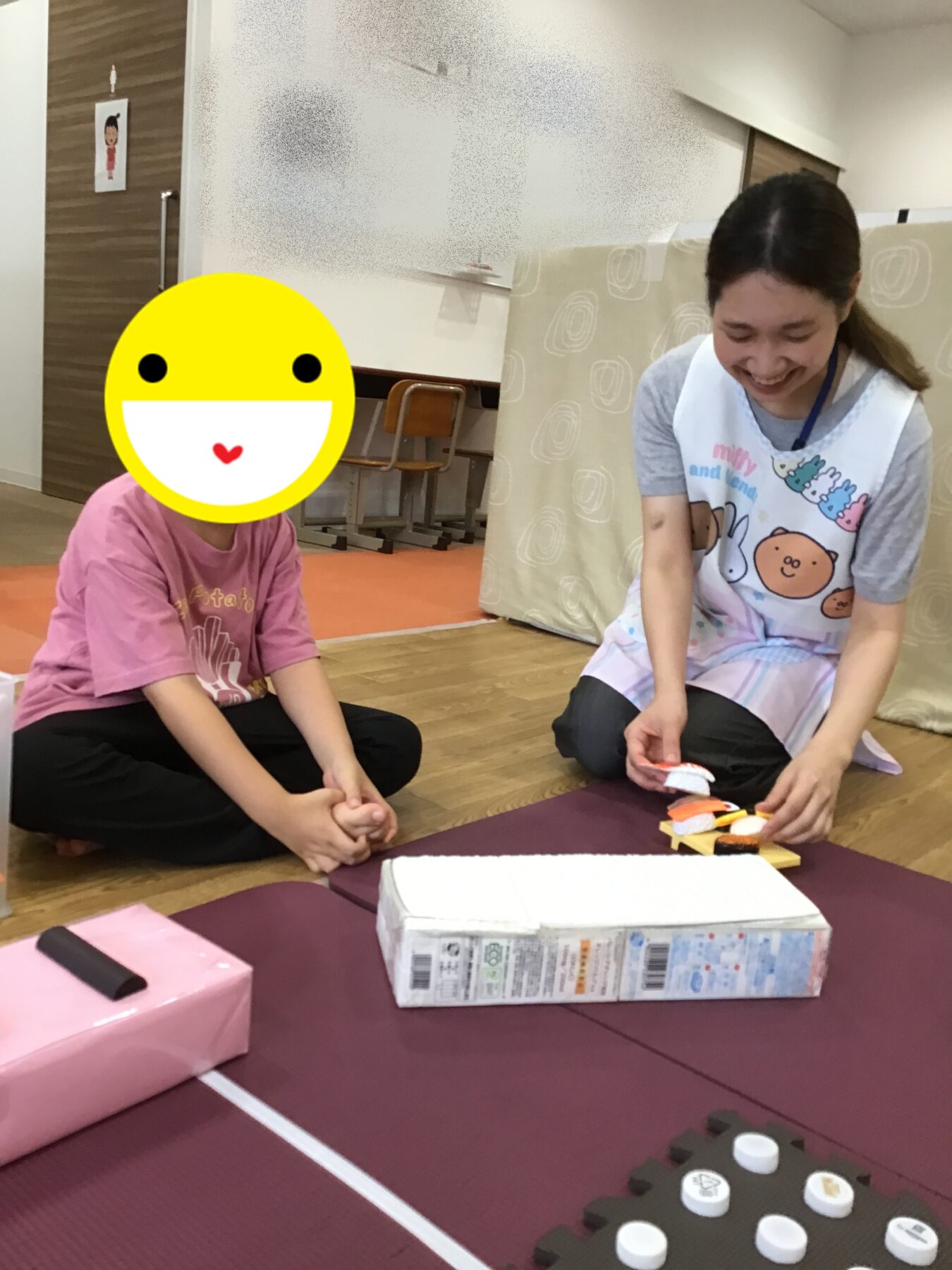 Caregiver and child sit cross‑legged on a purple mat, arranging colorful toy pieces in a play area.