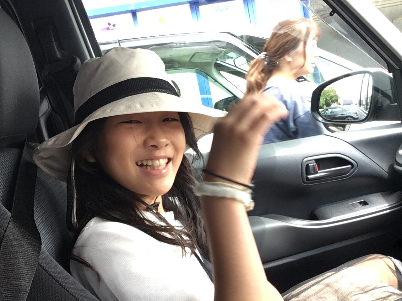 Smiling young girl in a white sun hat with a black band, sitting in a car.