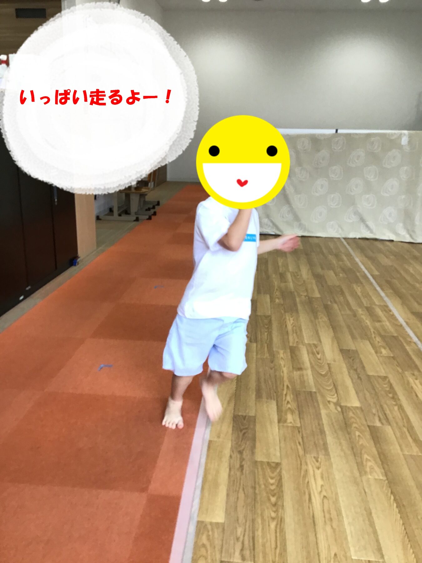 Child running indoors on an orange carpeted floor, with a yellow smiley-face overlay covering their face and red Japanese text on a white circle to the left.