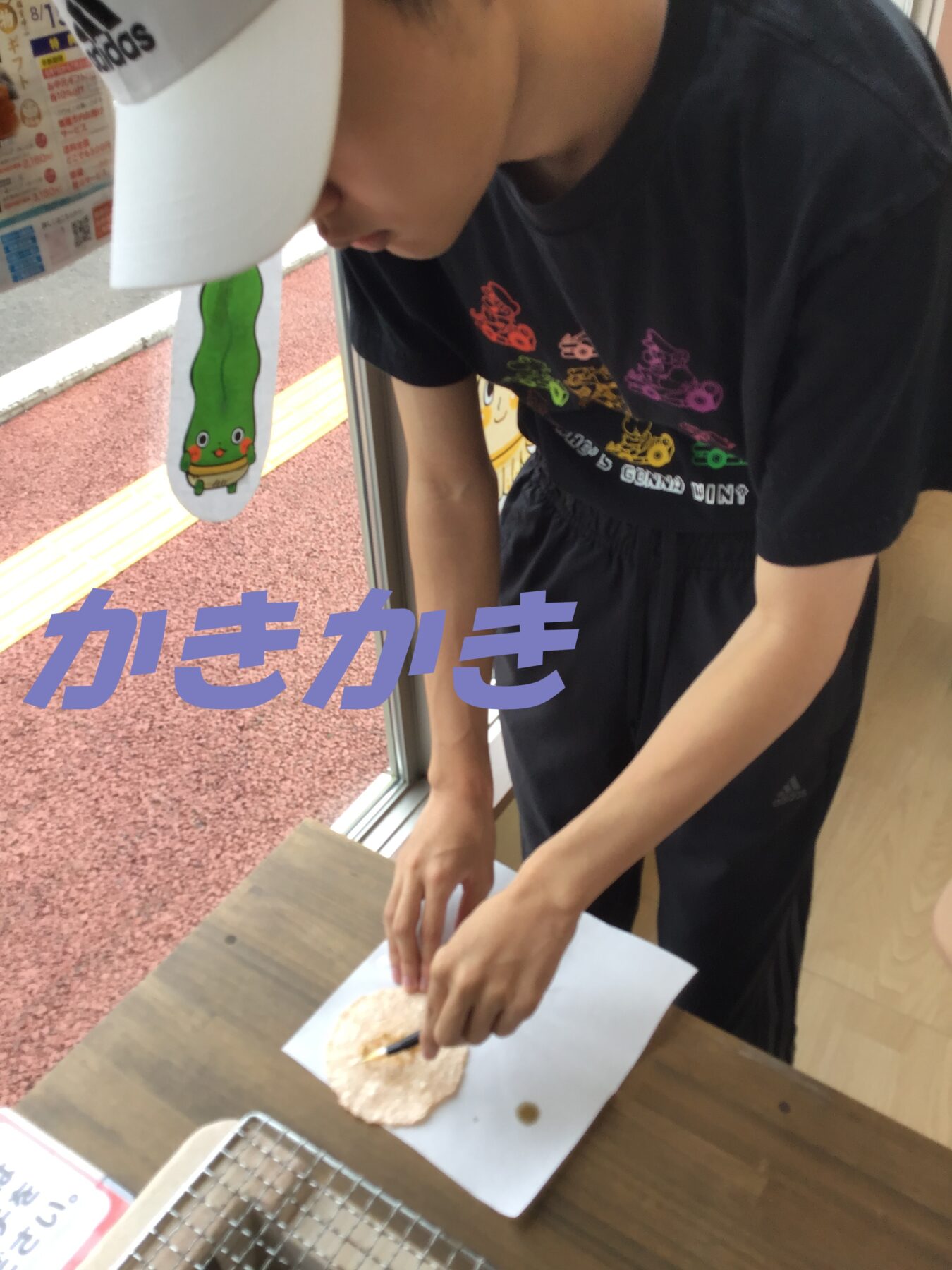 Person wearing a white cap and black shirt leaning over a table, pressing a round tortilla-like disk on parchment with a small tool during a hands-on activity in a bright room.
