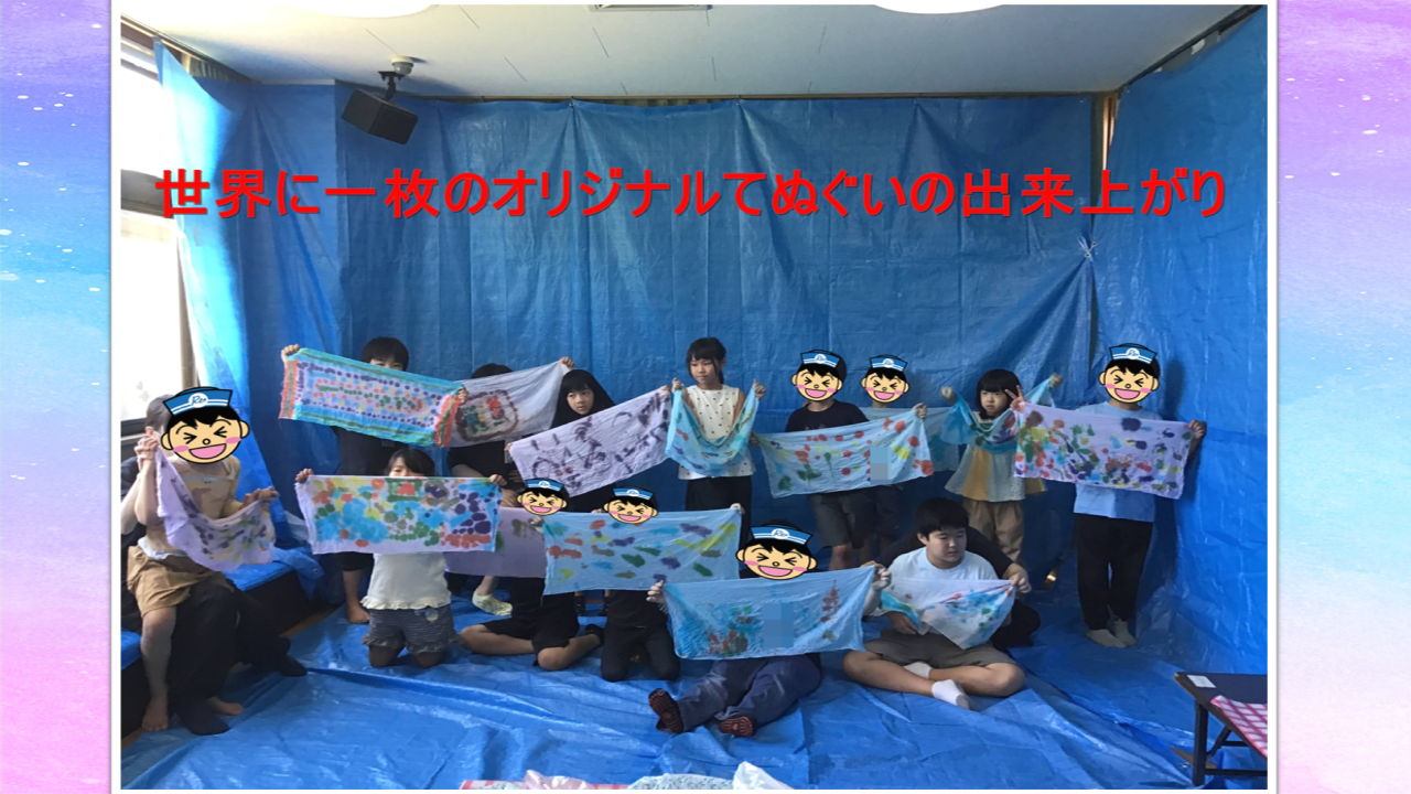 Group of children in a blue studio hold up their colorful handmade tenugui towels, showing off a group art project.
