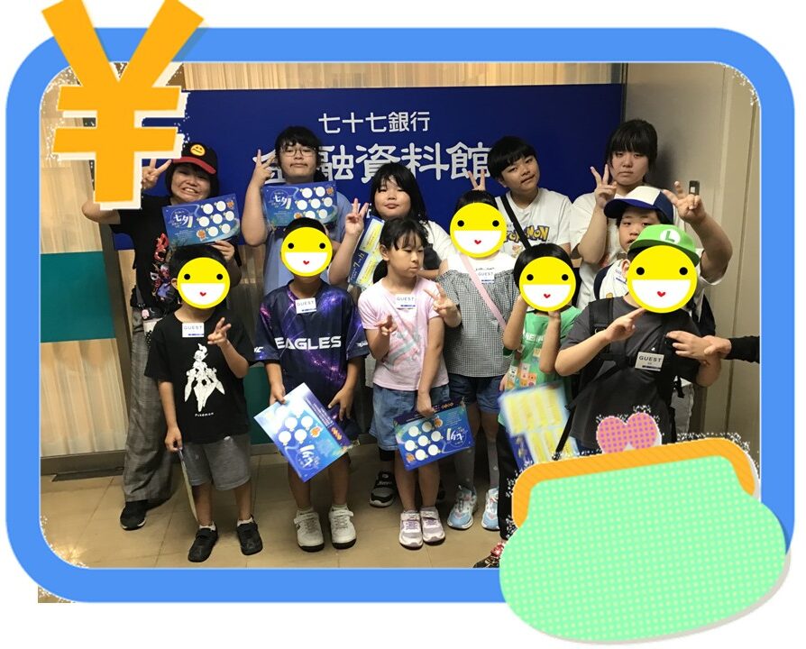 Group of children posing for a photo indoors, holding blue booklets, in front of a blue backdrop with Japanese text, faces covered with smiley stickers.