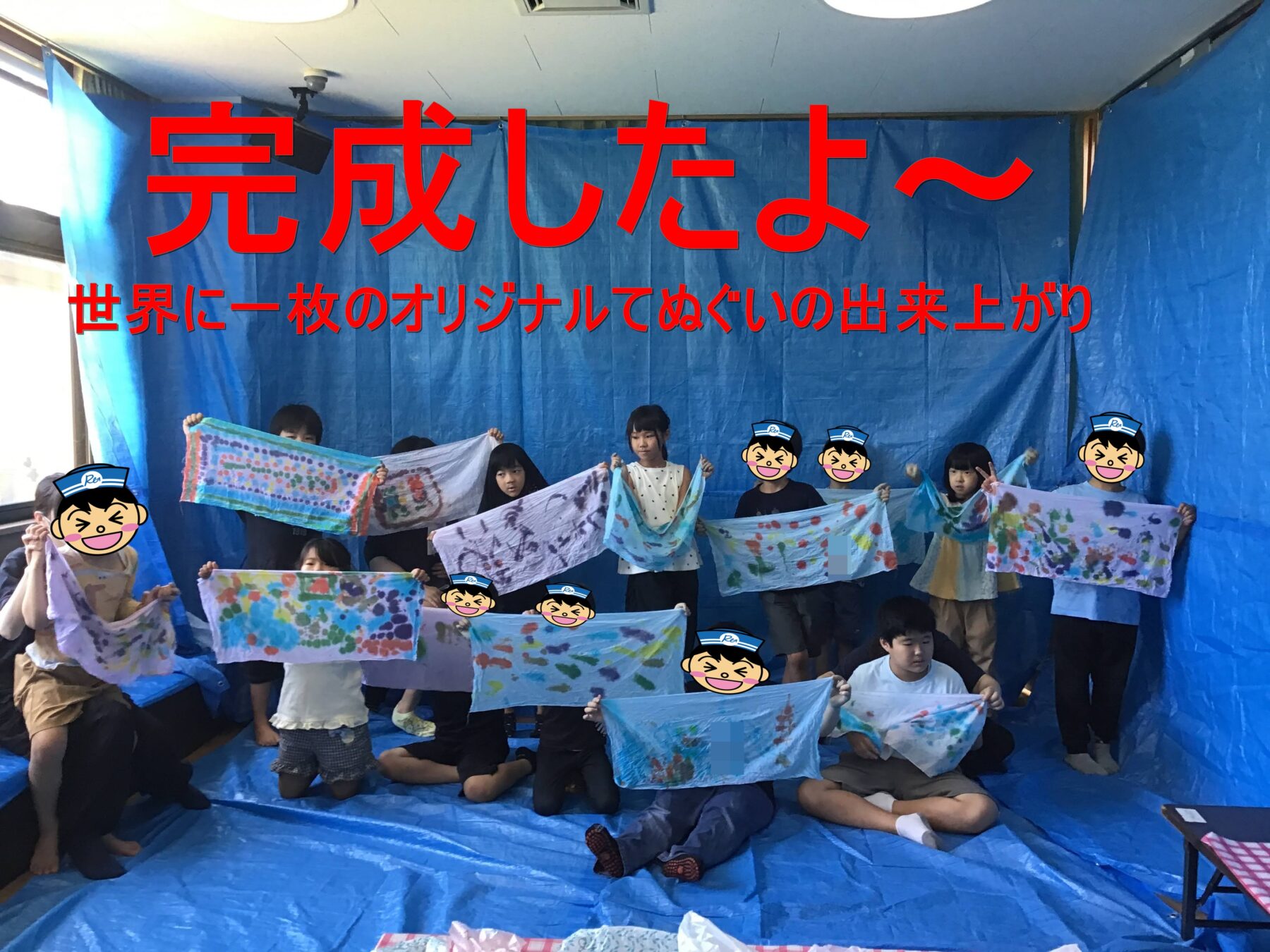 Children in a blue-walled room hold up colorful hand-painted cloths as a finished group art project.
