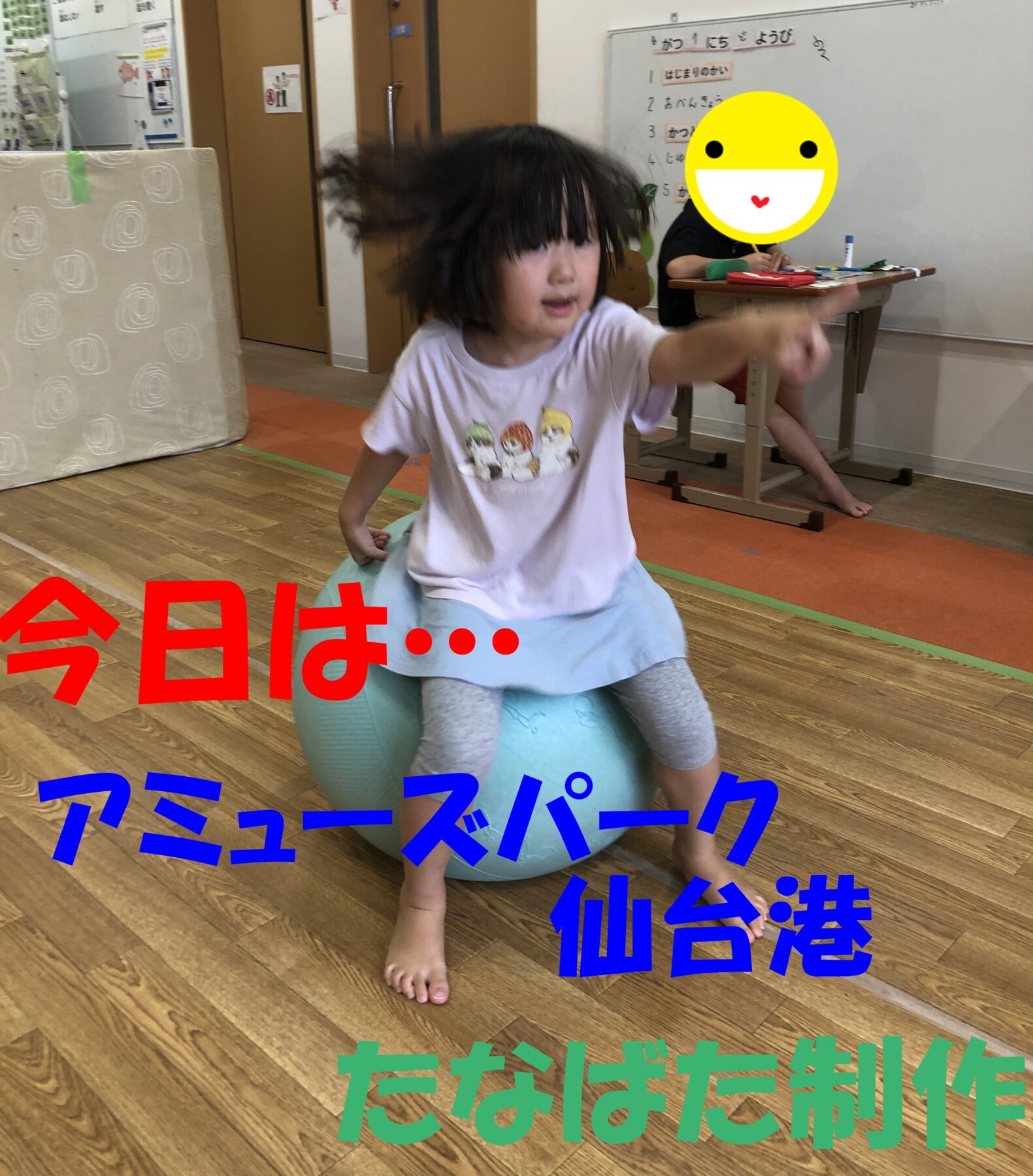 Child sits on a blue exercise ball in a classroom, arms raised for balance, hair moving as they bounce; large colorful Japanese text overlays cover parts of the scene.