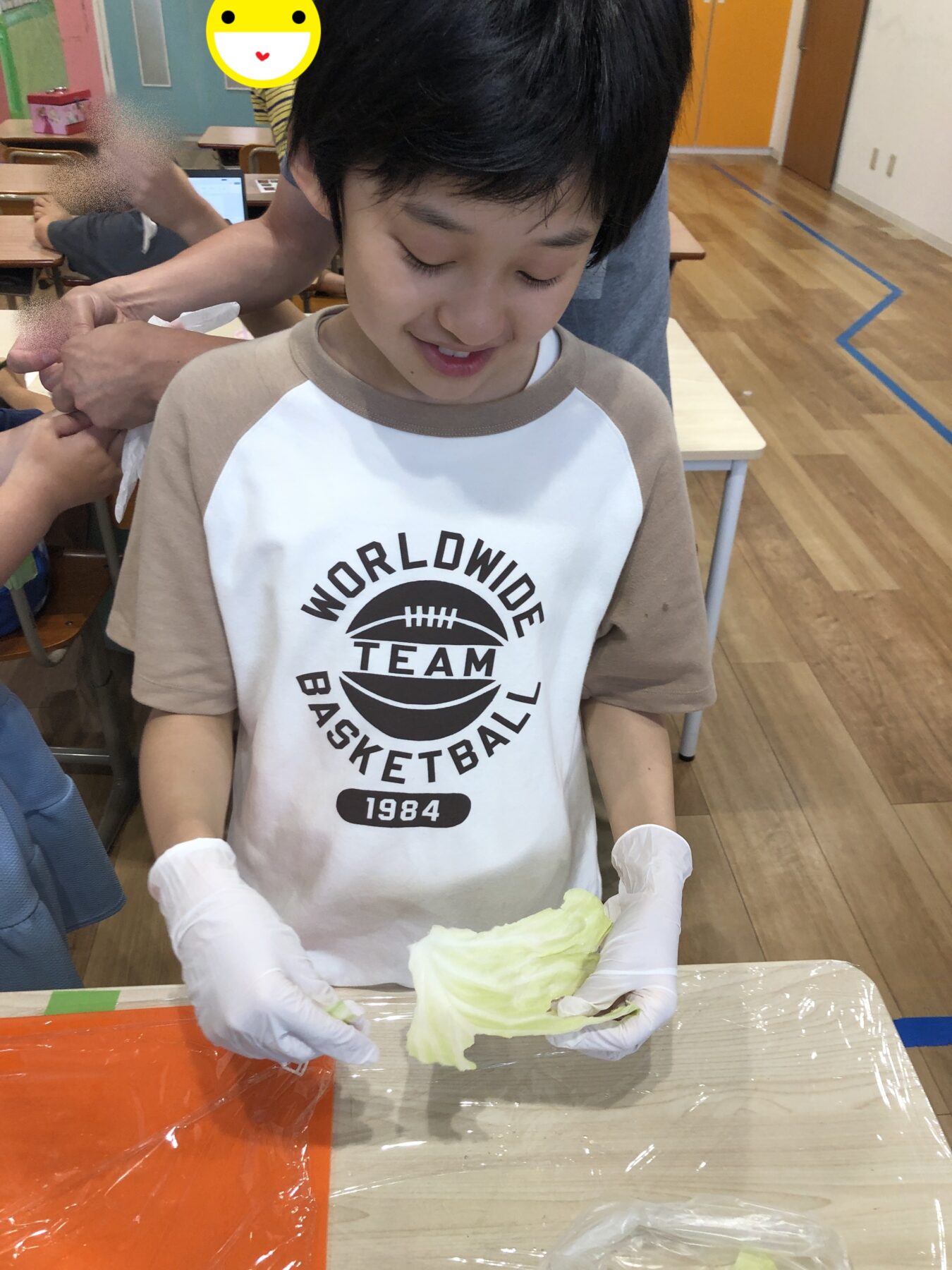 Boy wearing gloves holds a head of cabbage at a classroom table during a hands-on activity.
