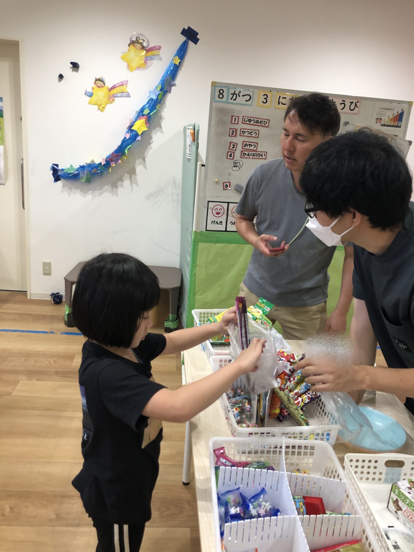 Child hands candy from a basket to an adult wearing a mask at a table in a classroom.