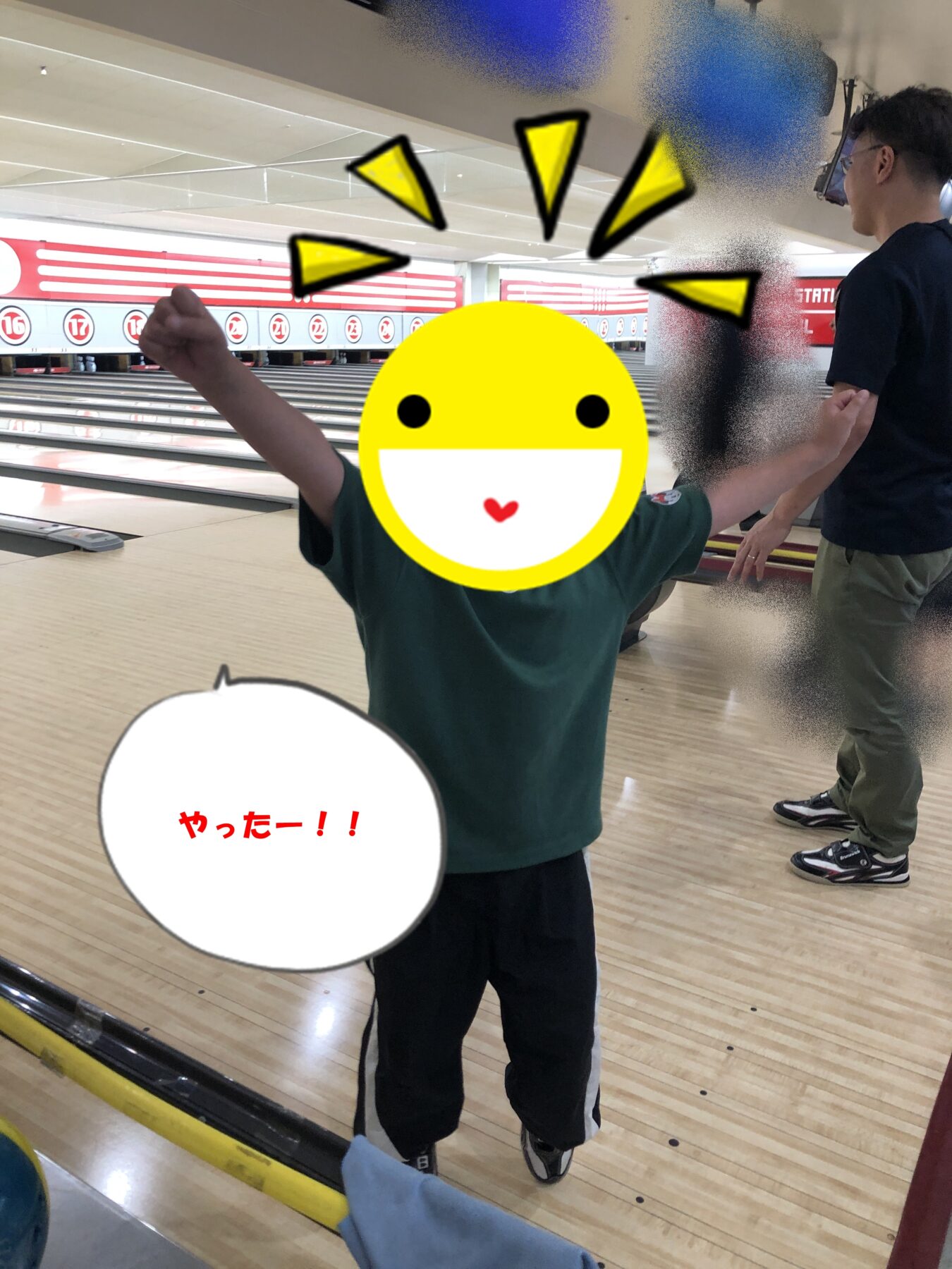 Child at a bowling alley with arms raised in celebration; a large emoji covers their face, background lanes and another person nearby; speech bubble reads 'やったー!!'