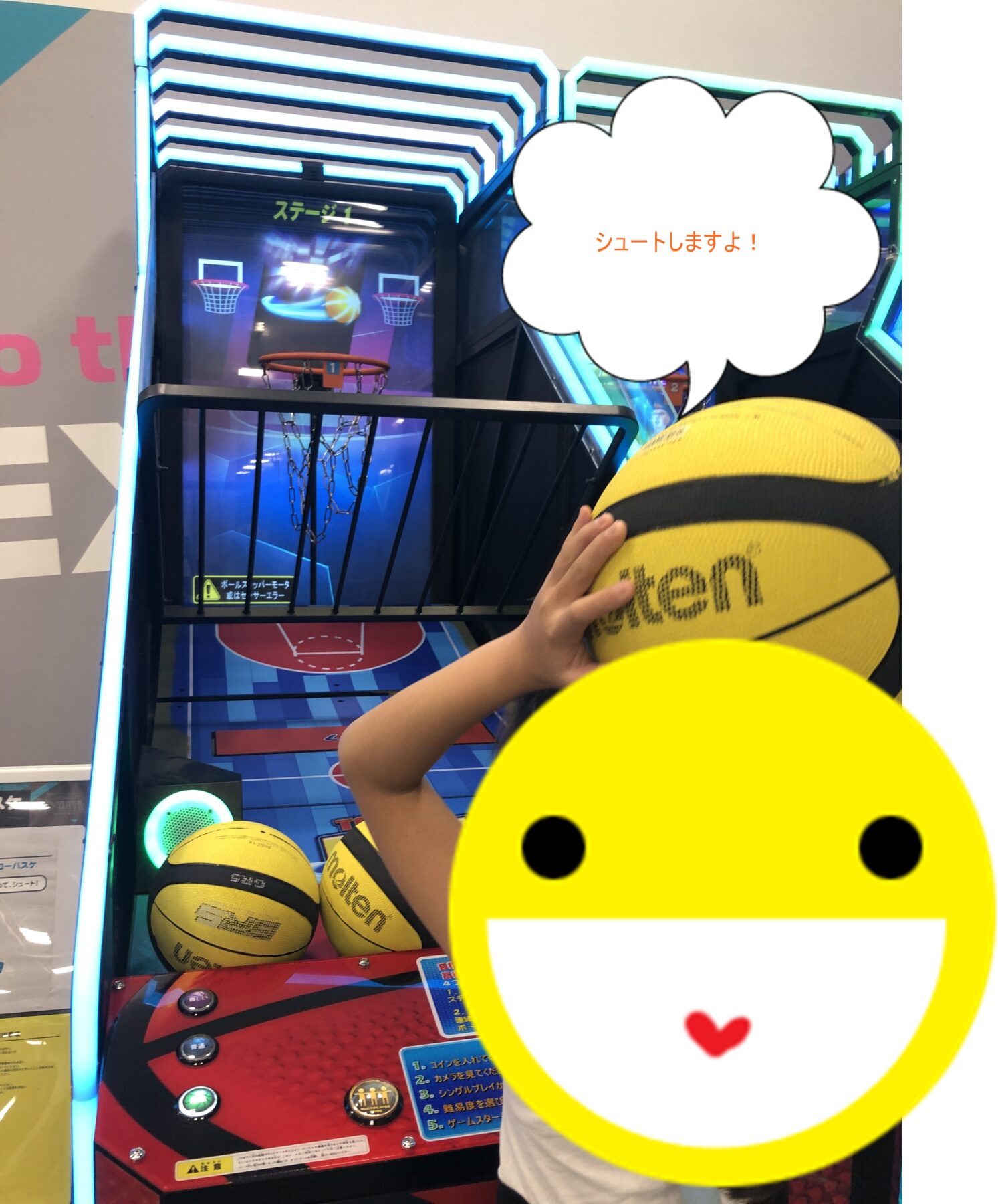 Arcade basketball game with neon blue framing; child holds a yellow basketball toward the hoop, while a large yellow smiley sticker covers part of the view.
