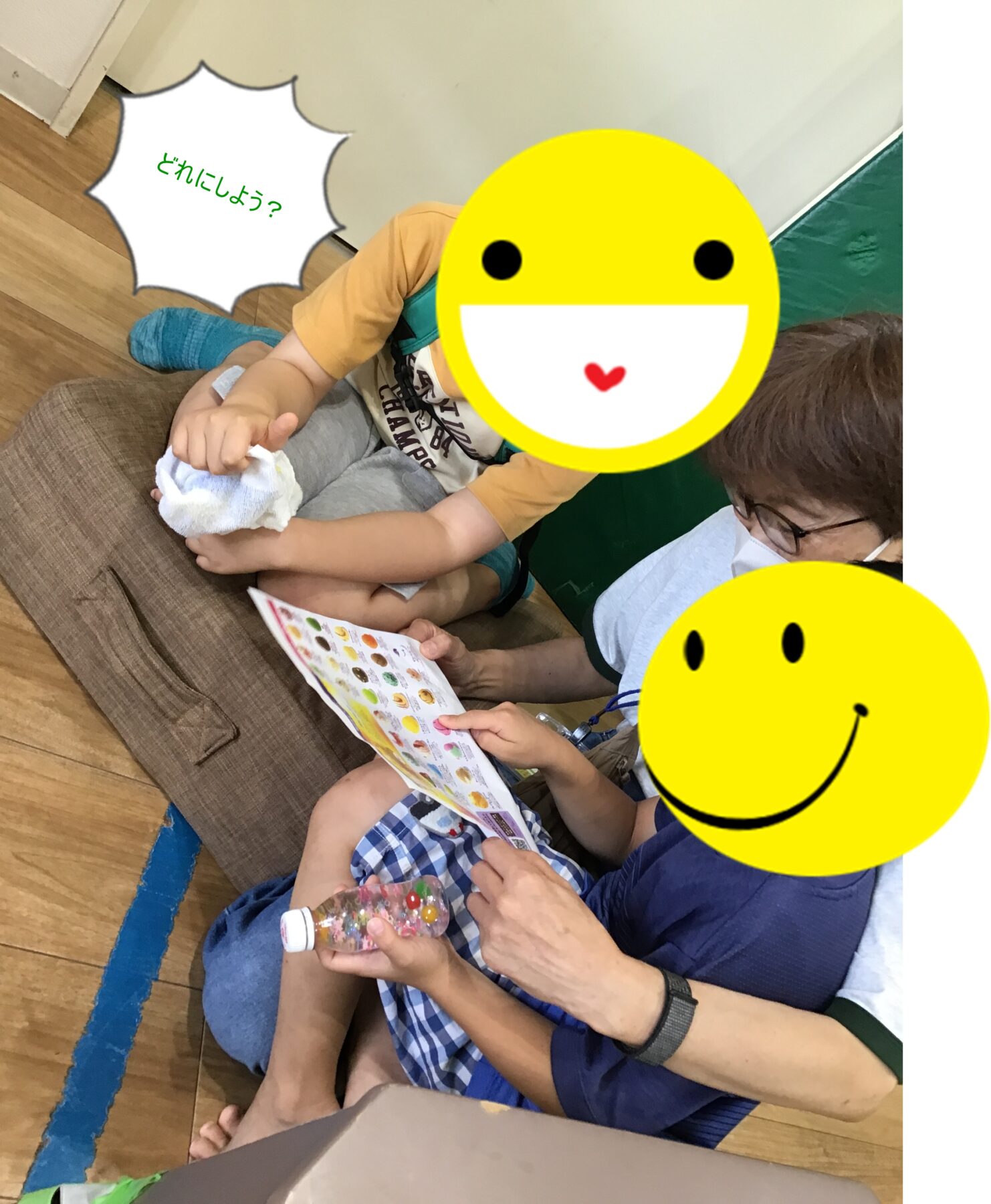 Children and an adult sit on the floor examining a colorful activity sheet; faces are covered by large yellow emoji stickers.