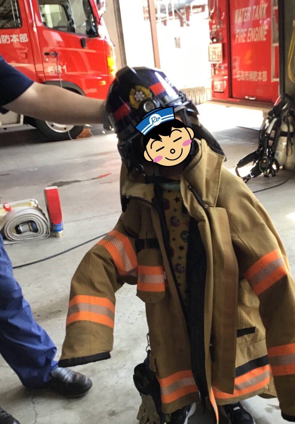 Firefighter in full turnout gear kneels on the workshop floor, with red fire trucks and equipment in the background.