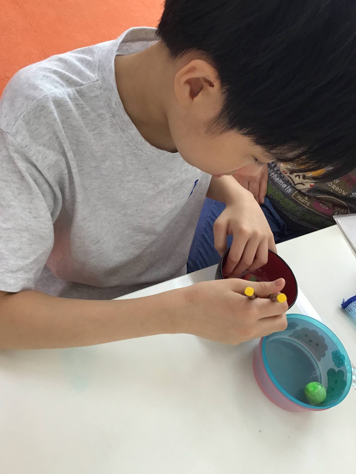 Child focused on a craft activity, inserting yellow pegs into a red circular lid at a white table.