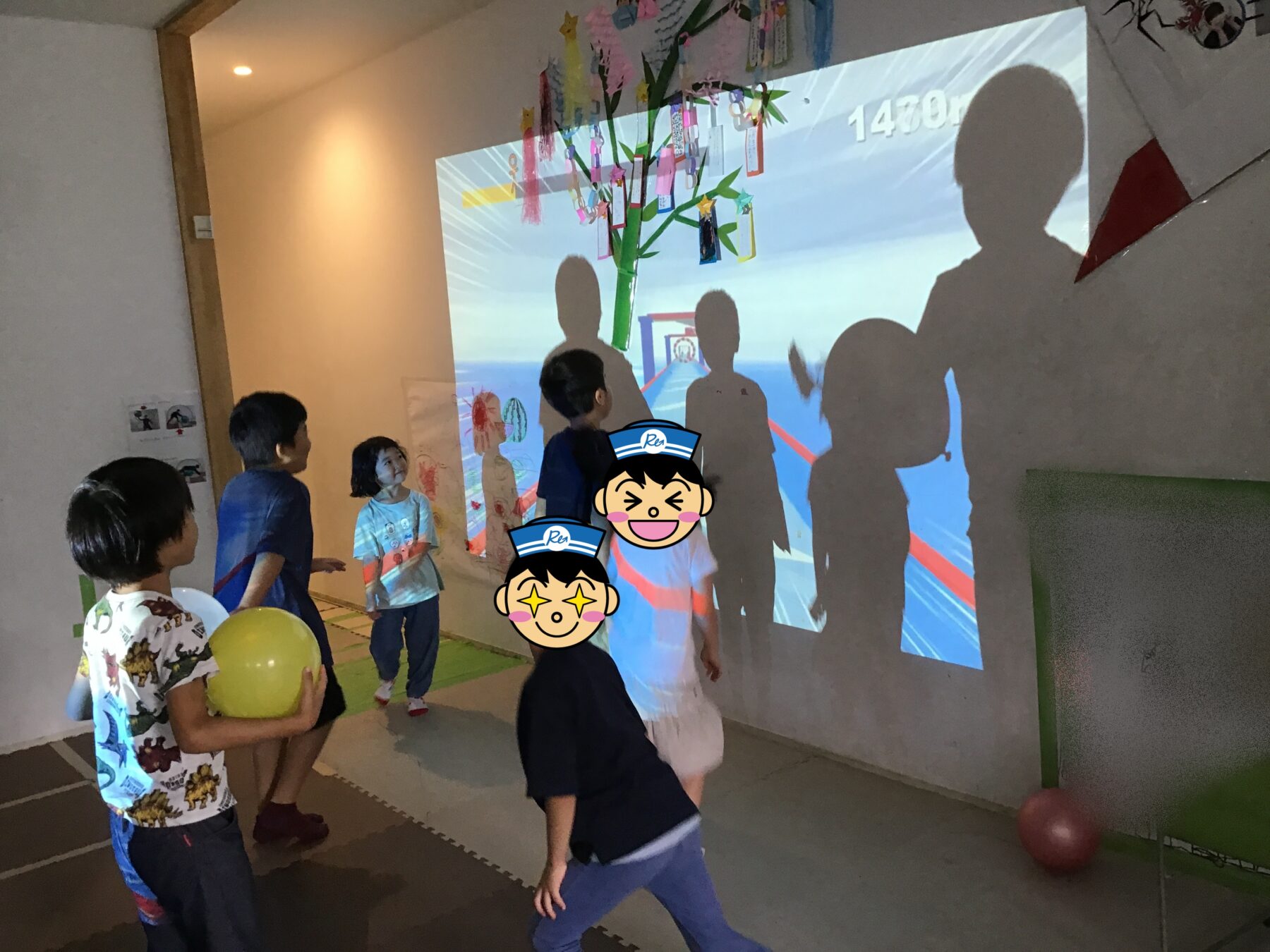 Children standing and watching a large interactive projection on the wall, showing a stylized tree with hanging cards against a blue background and their shadows.