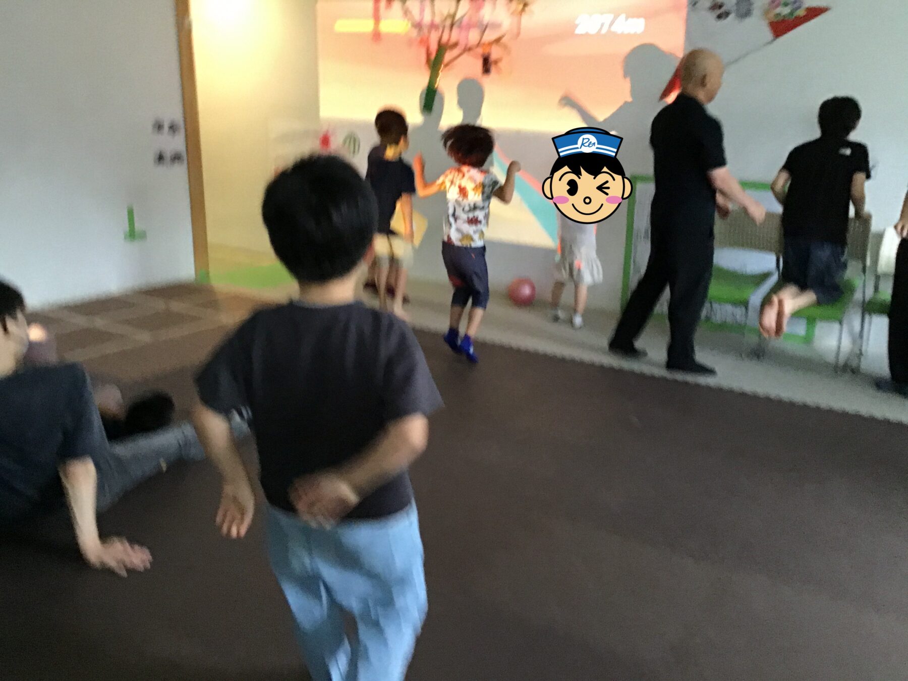 Children playing indoors near a colorful wall mural, with an adult supervisor in black nearby.