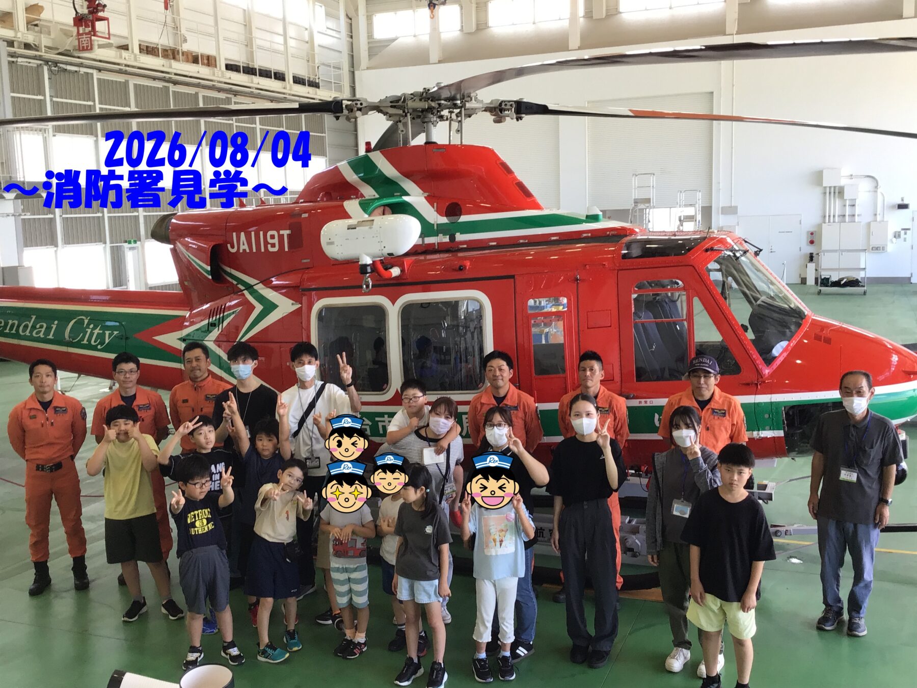 Group of children and adults posing in front of a red firefighting helicopter inside a hangar, some in orange uniforms and wearing masks.