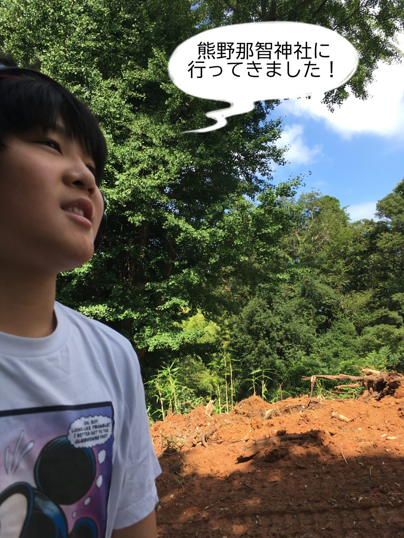 Person outdoors with trees behind, wearing a white shirt and headphones, speech bubble reading '熊野那智神社に行ってきました！' (I went to Kumano Nachi Shrine!).
